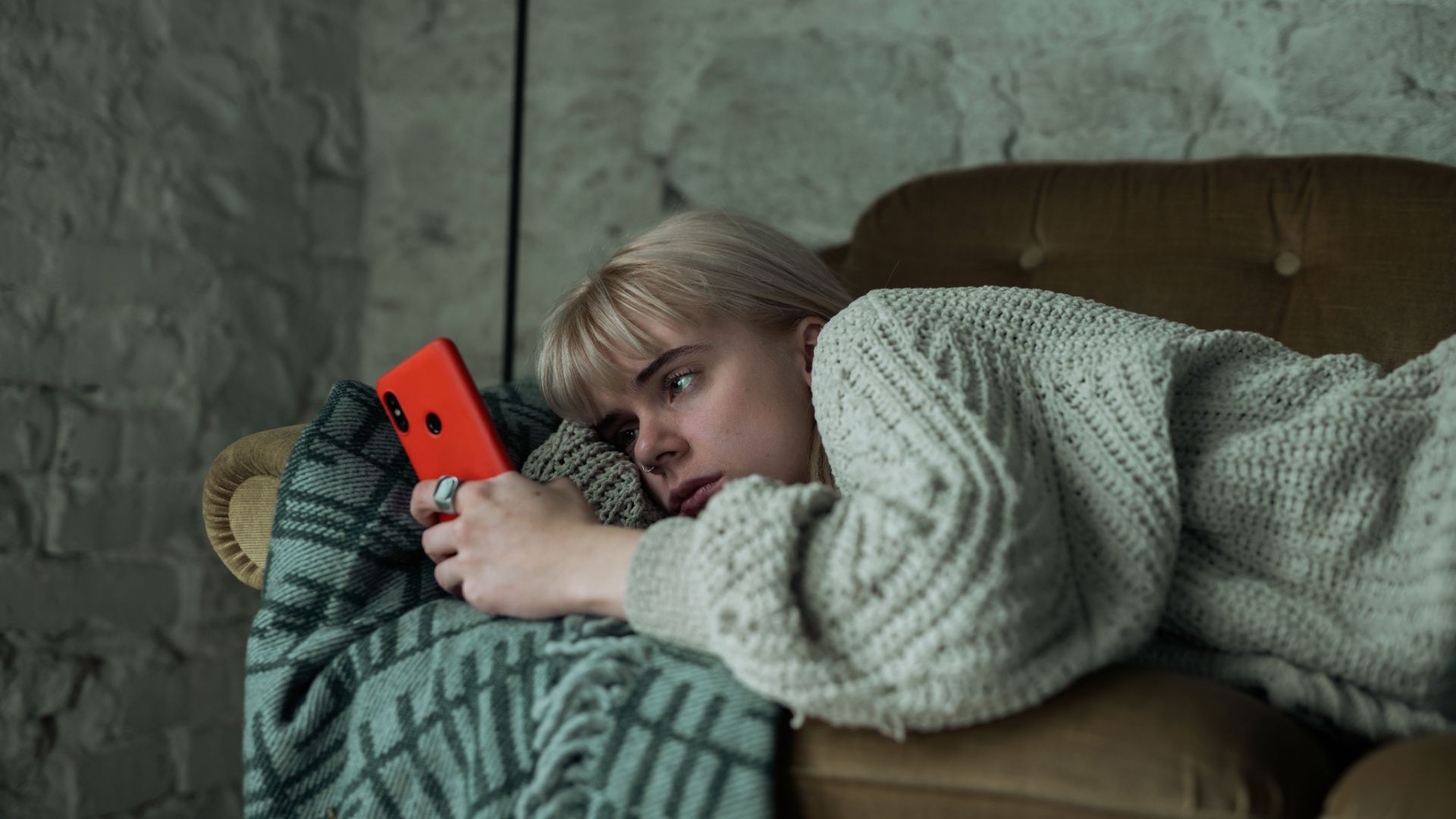 Woman lying on a sofa staring at a smartphone.