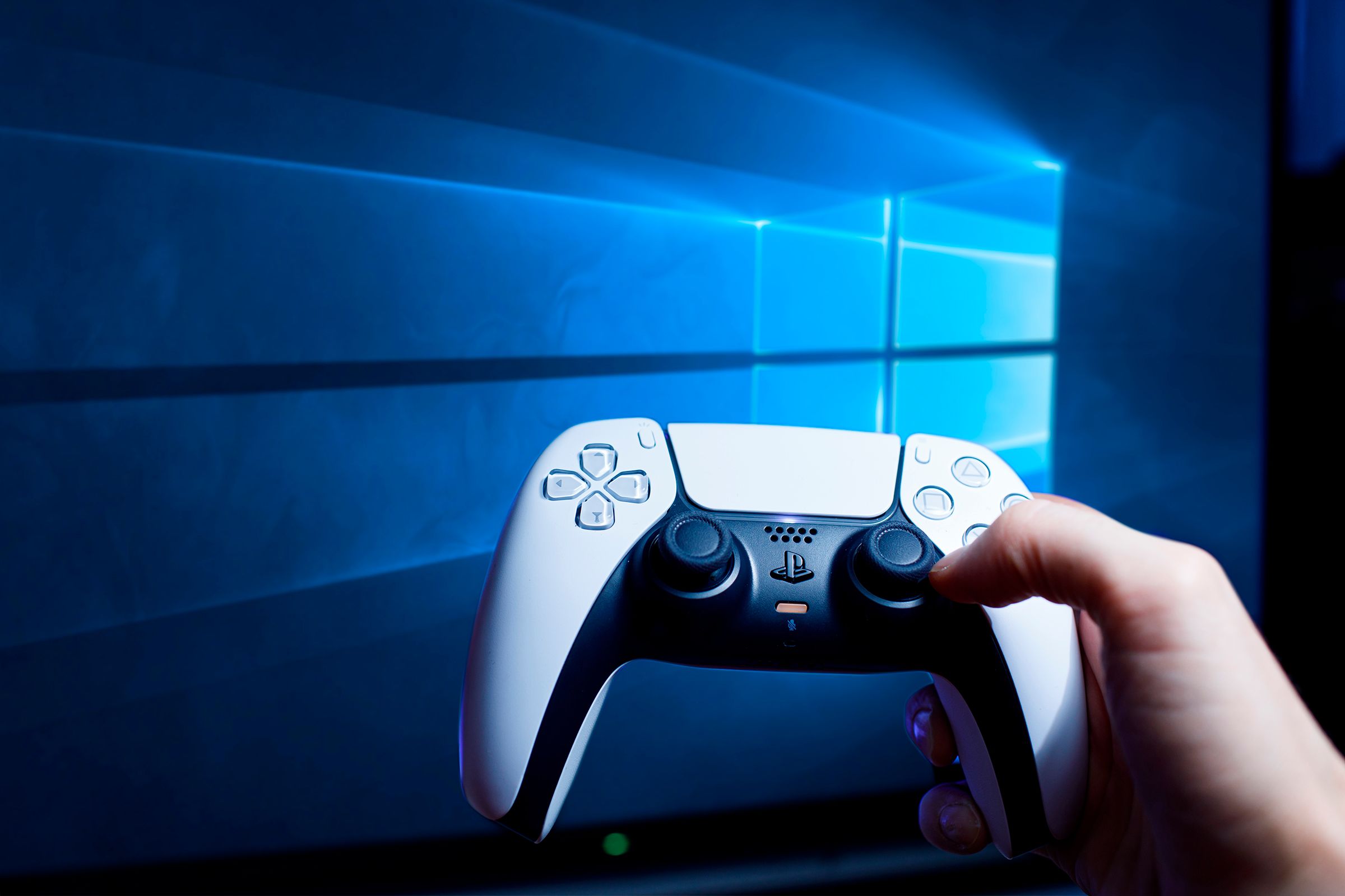 A hand holding a PS5 controller with the Windows 10 screen in the background.