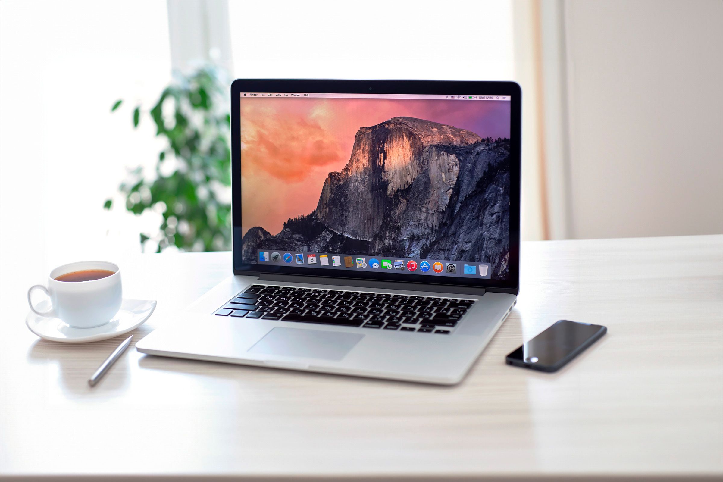 A Macbook on a table with a cup on the left side and an iPhone on the right side.