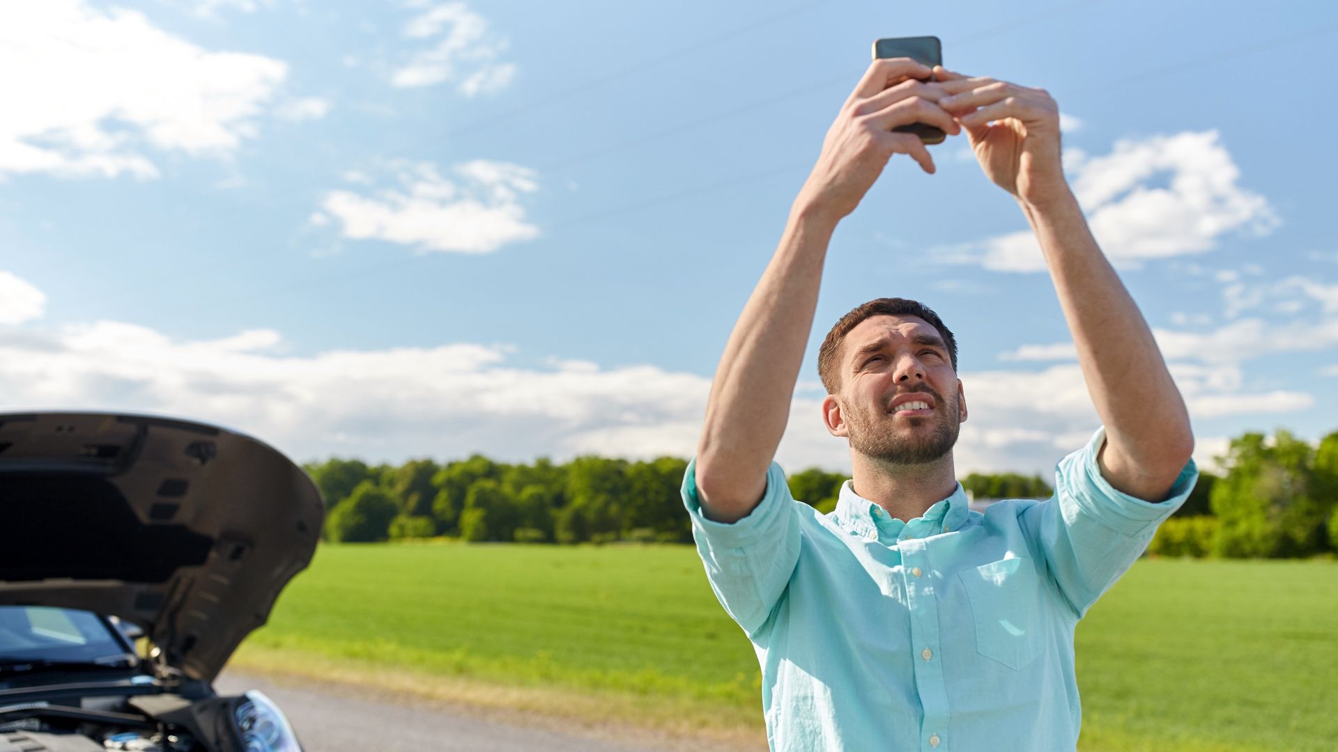 man holding a phone up high trying to get signal.