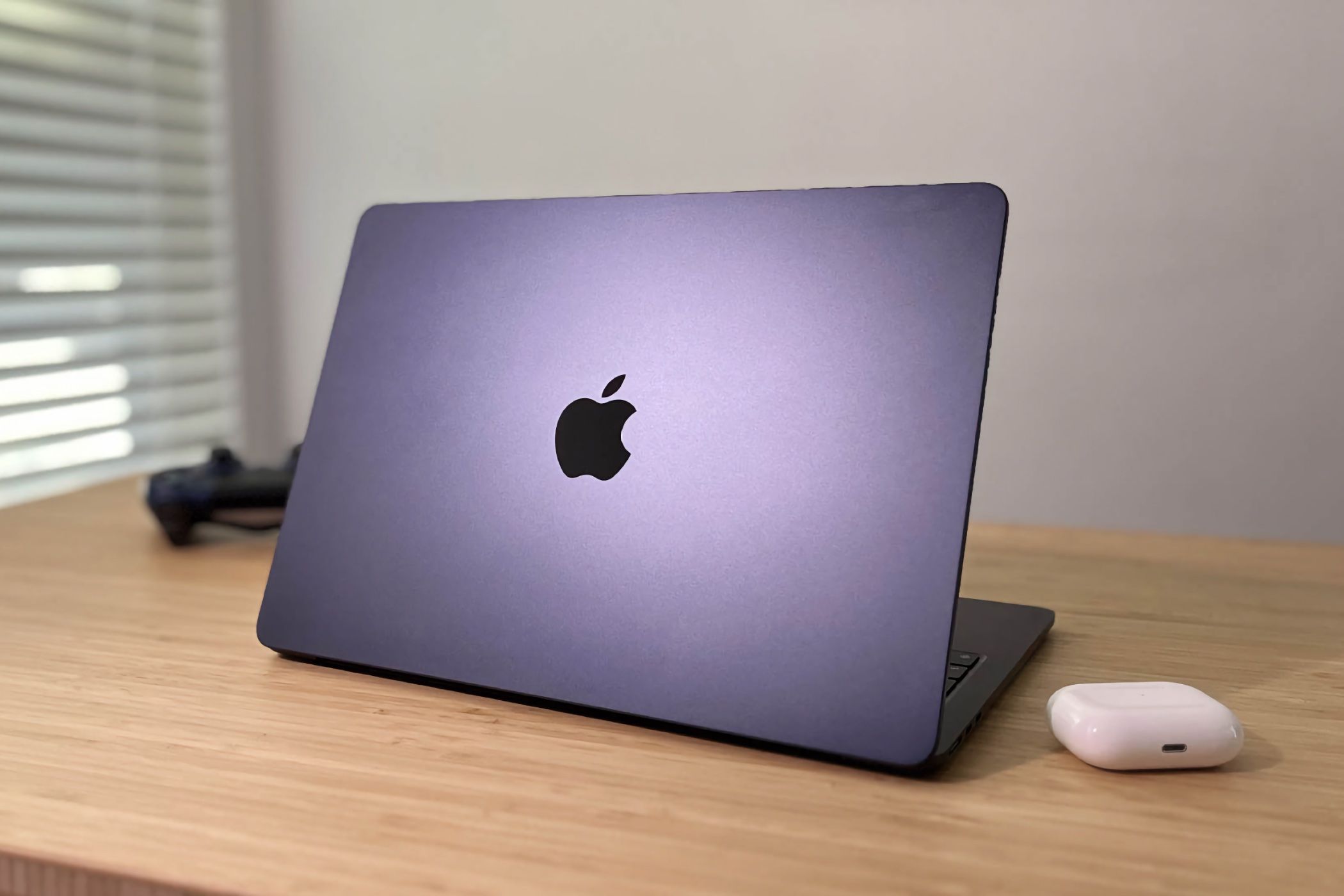 Apple MacBook Air M2 resting on desk next to AirPods Pro and PS4 controller.