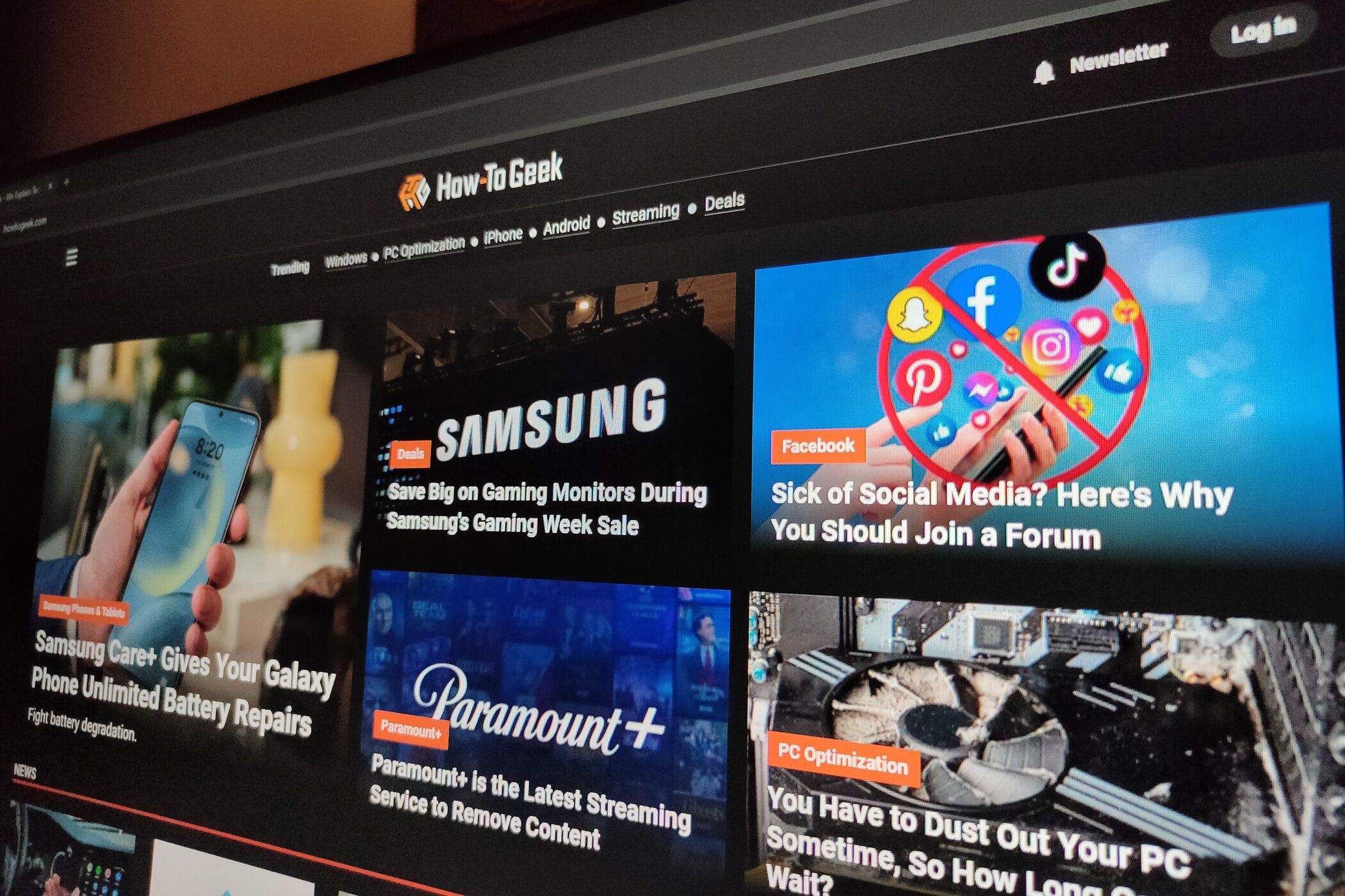 The How-To Geek website in dark mode shown on a monitor in a dimly lit room.