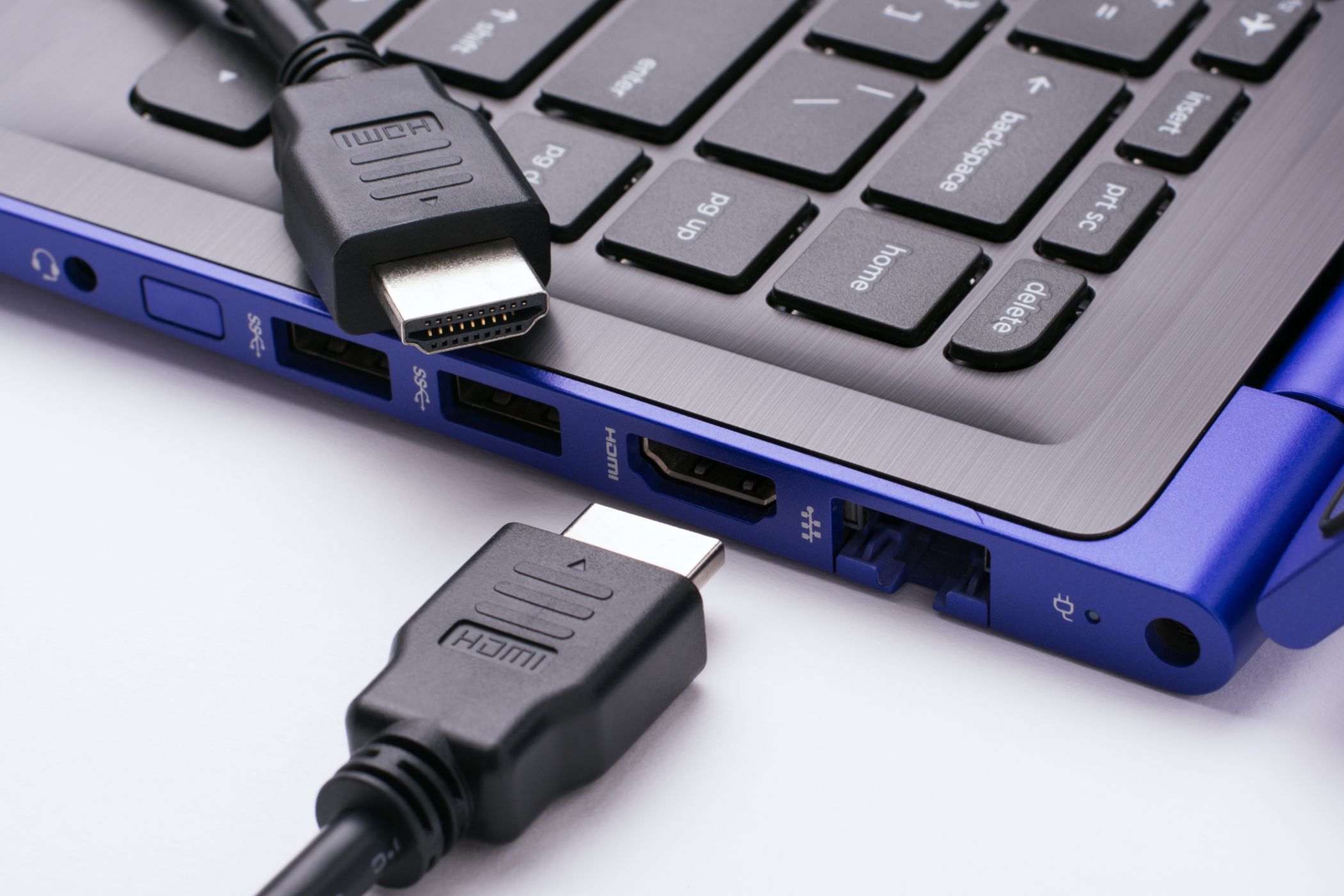 Two ends of the HDMI cable near the HDMI port of the modern blue laptop on a white background.