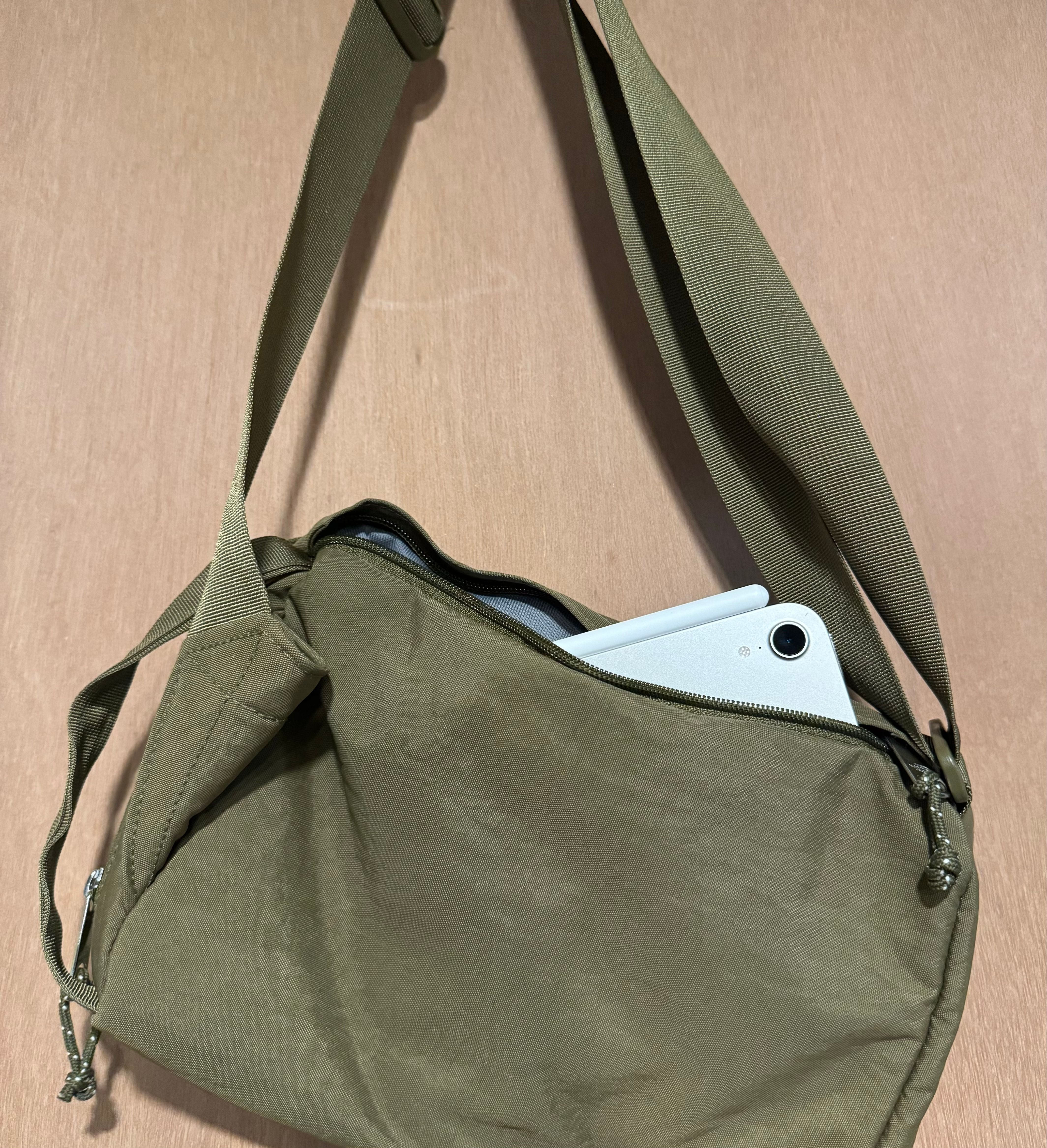 An iPad mini peeking out of a green crossbody bag.