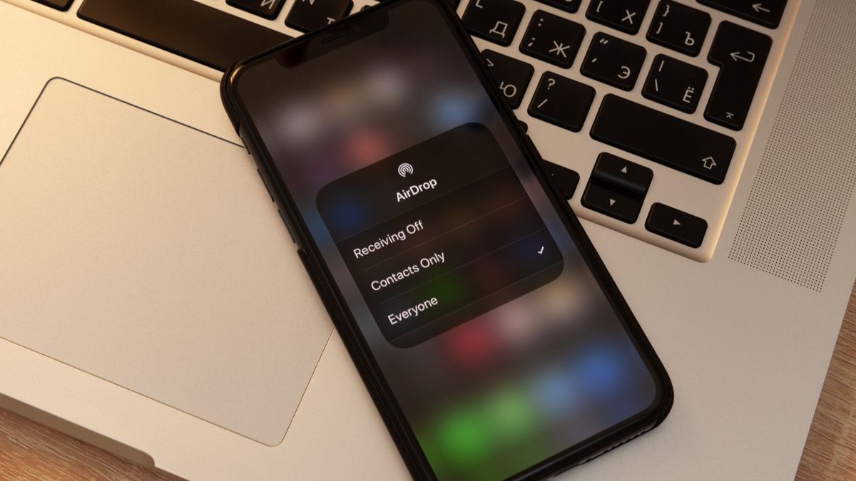 An iPhone showing an AirDrop prompt and resting on top of a MacBook.