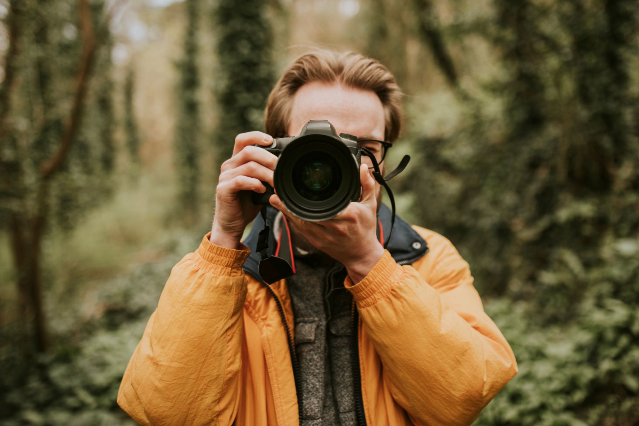 Male photographer in the woods pointing a camera.