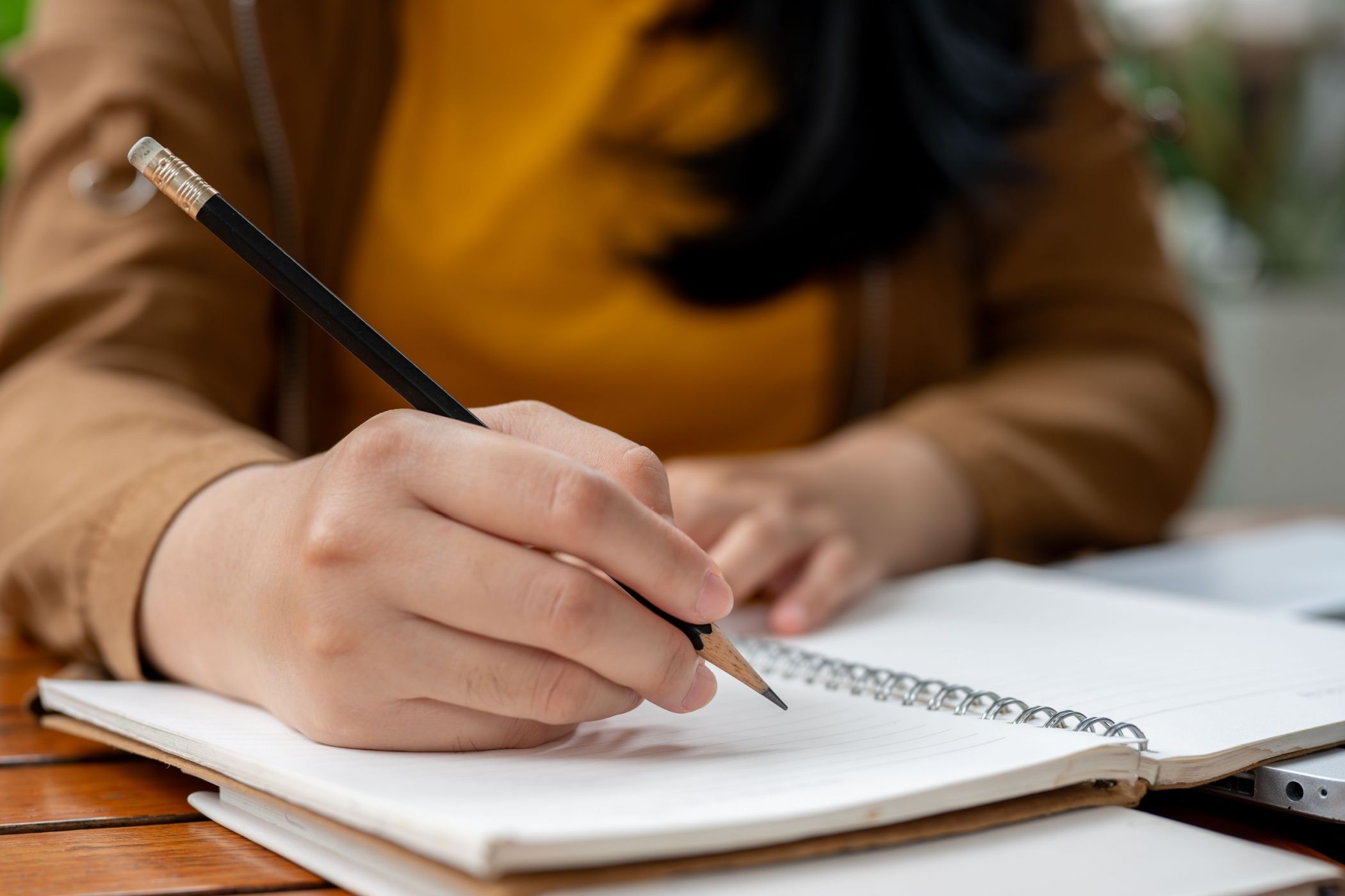 A close-up image of a woman holding a pencil, writing something in her notebook