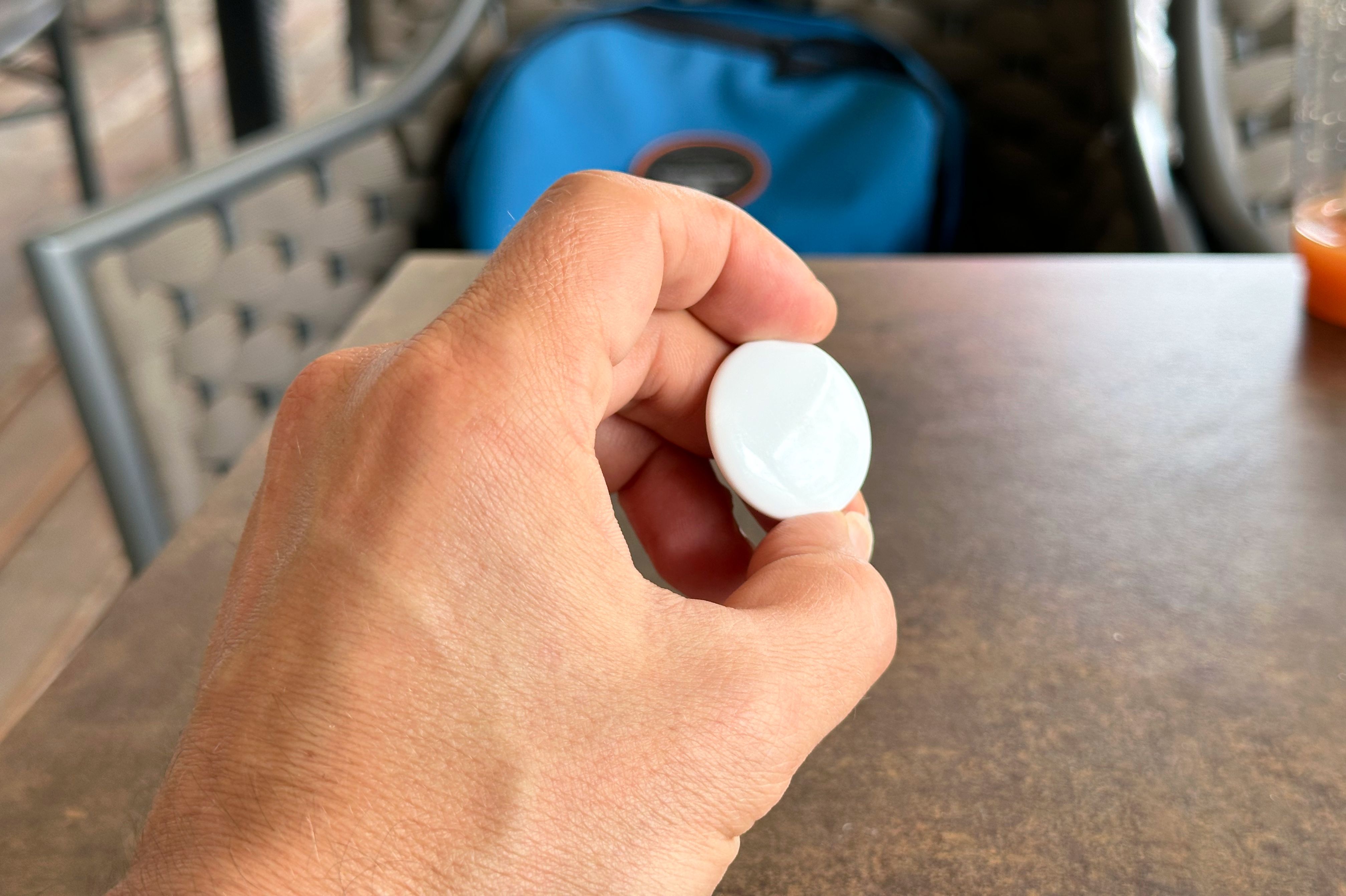 Male hand holding an Apple AirTag between thumb and index finger.