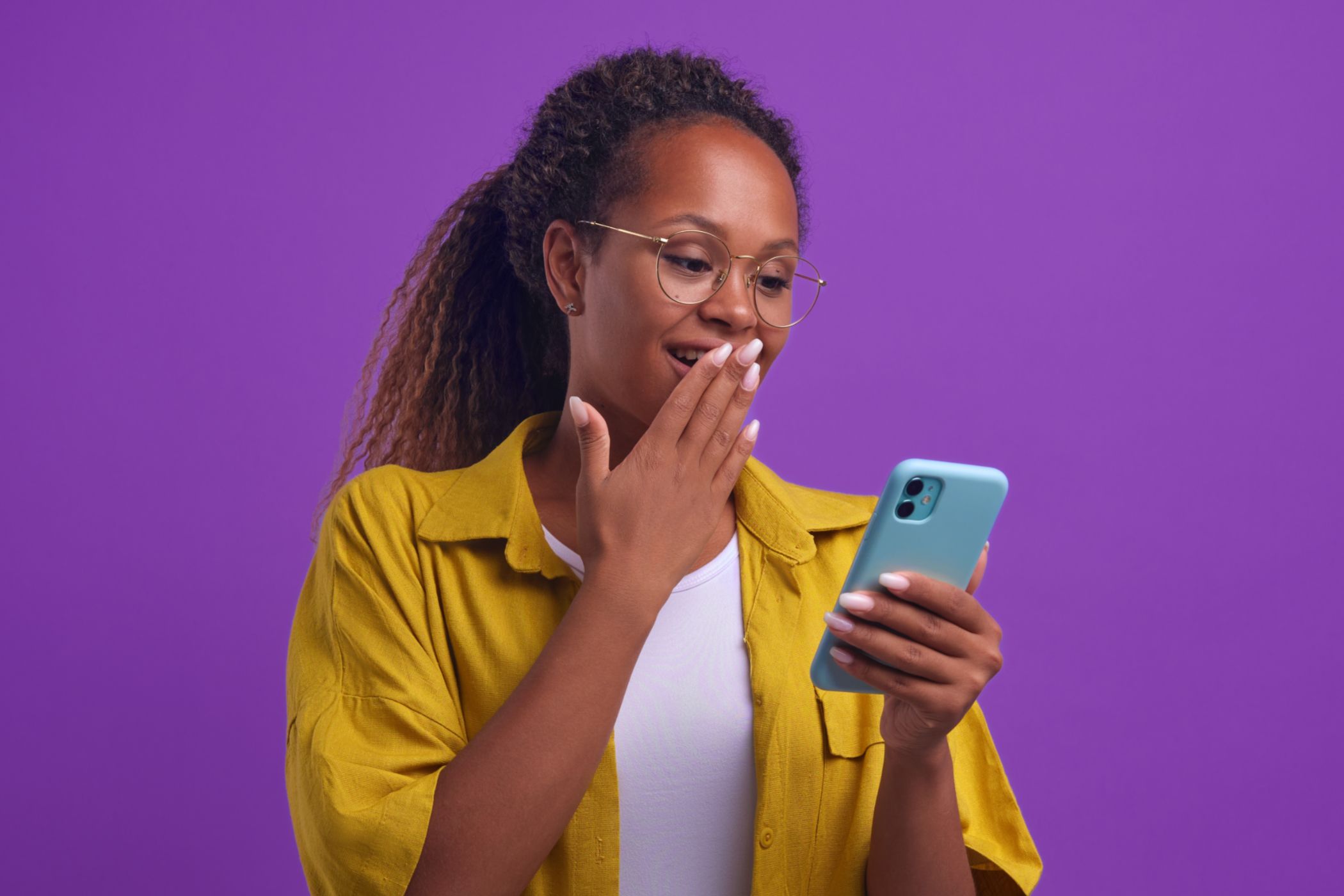 A young woman covering her mouth while holding an iPhone.