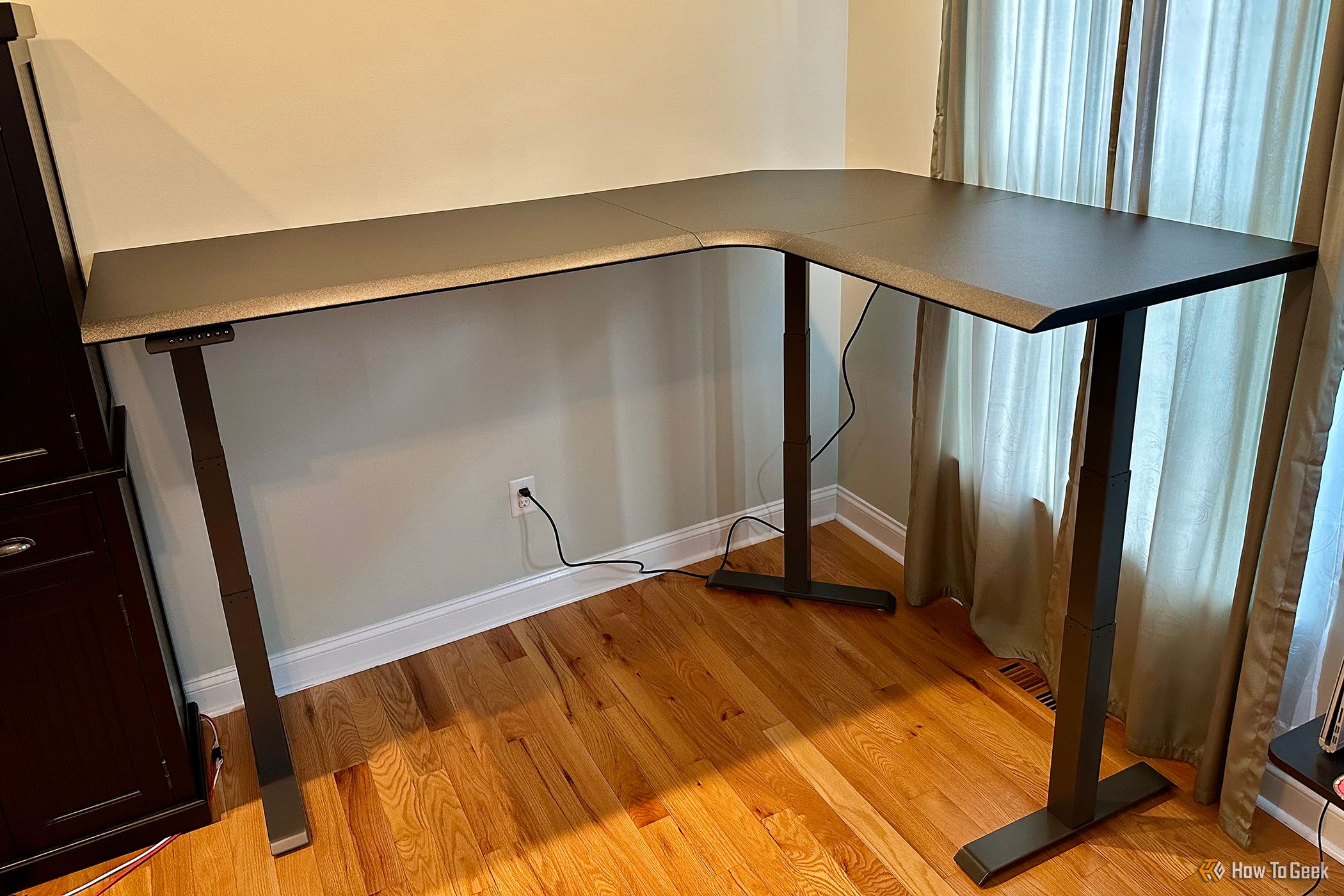 Vari L-Shape Electric Standing Desk in a corner by a window