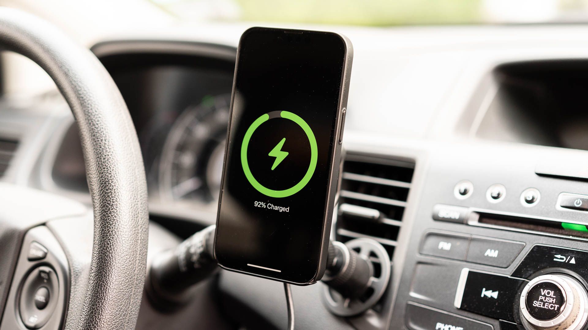 An iPhone charging on a car's vent mount.