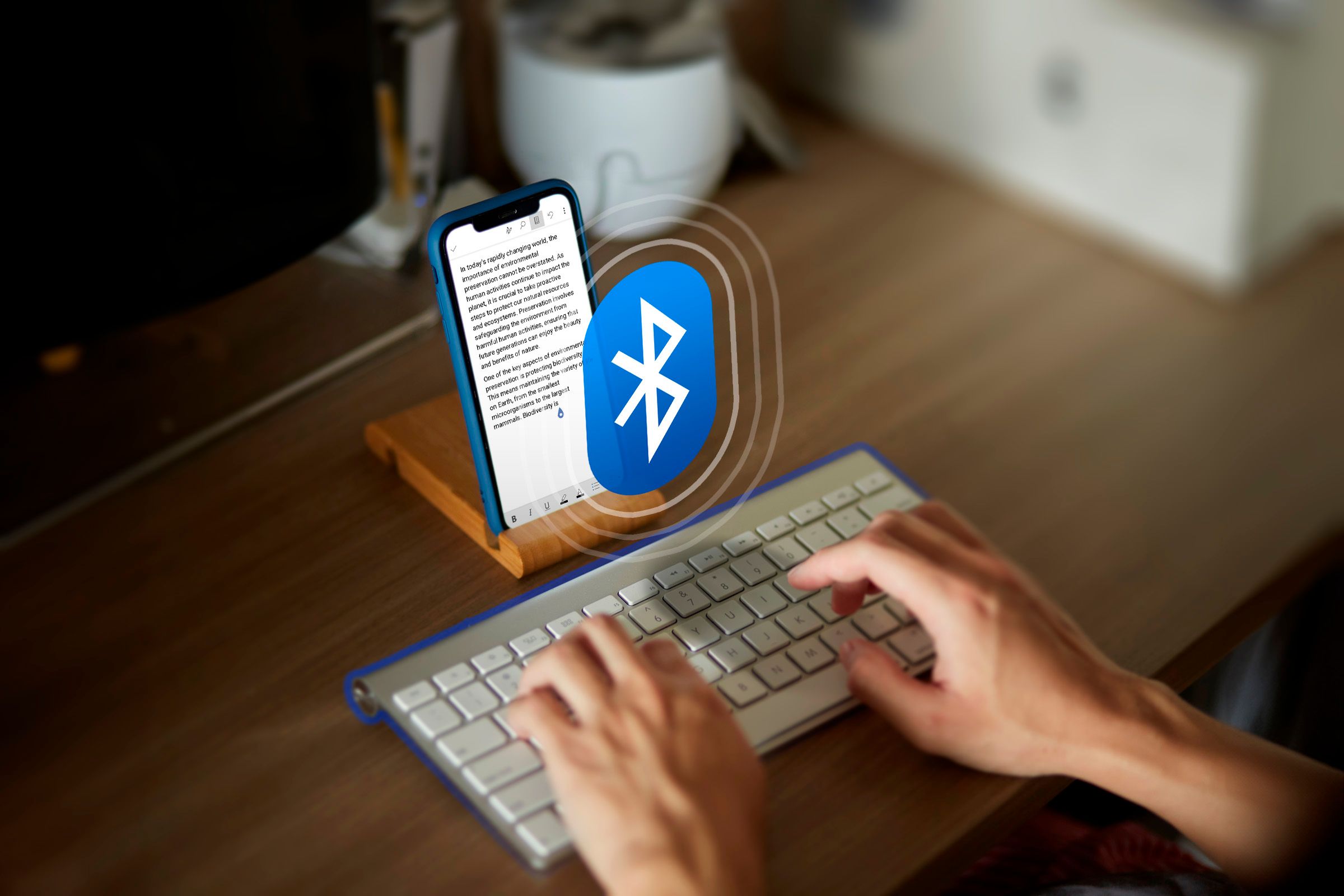 A person typing a text on their phone using a Bluetooth keyboard with the Bluetooth icon in the center.