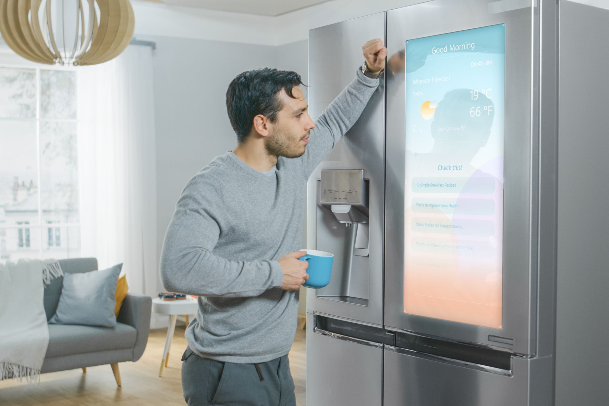 Man leaning against a smart fridge showing weather on the screen.