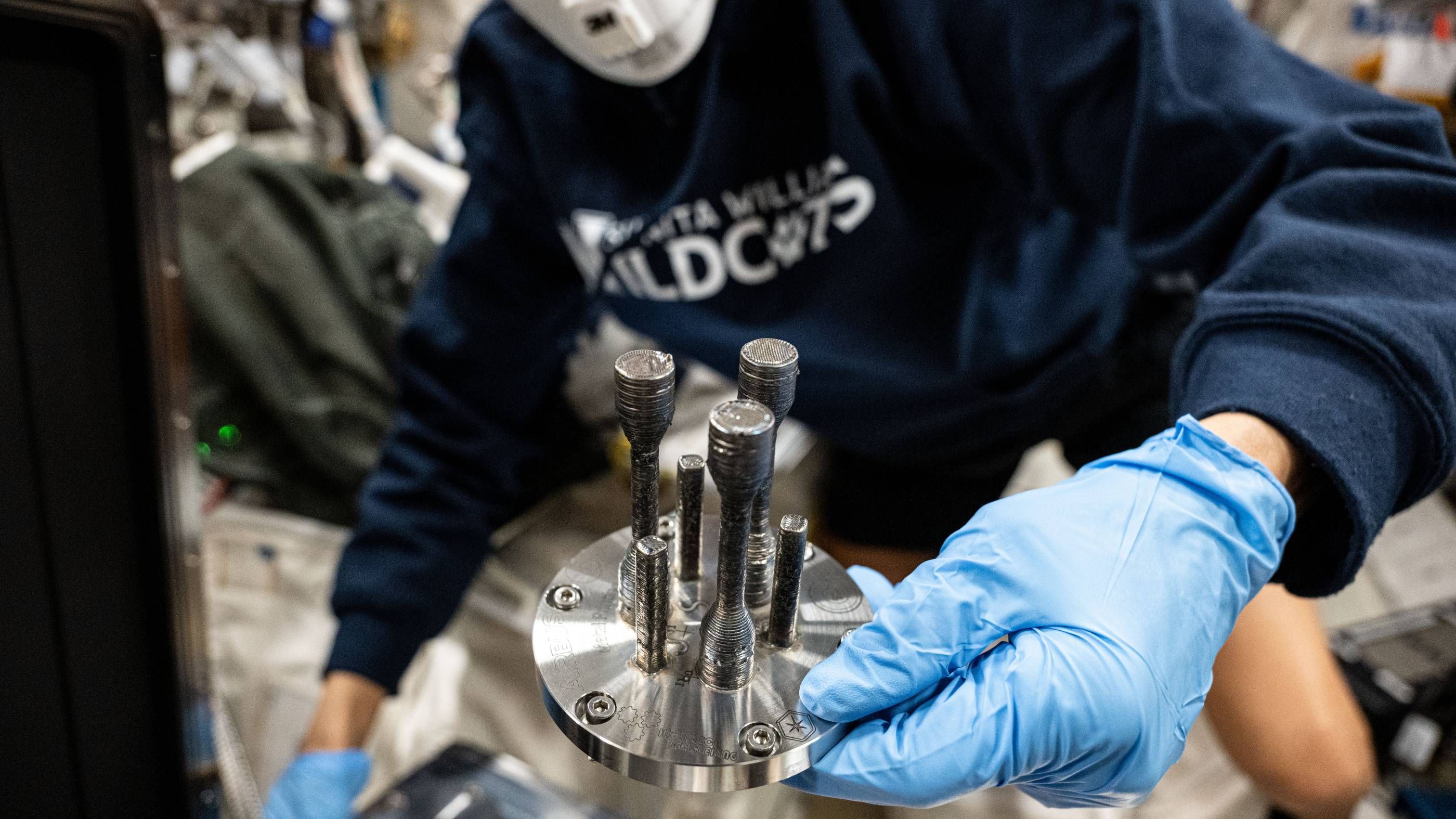 An astronaut holding the first metal object 3D printed in space