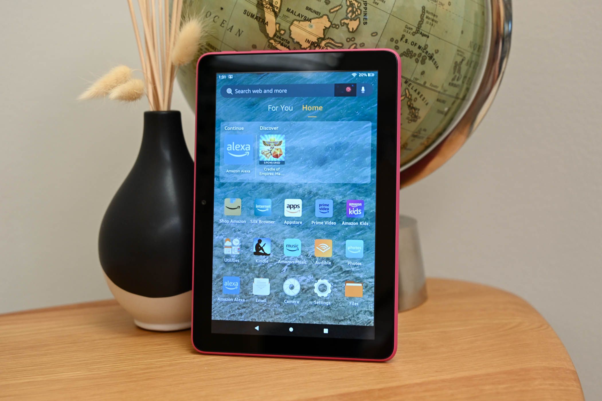 The Amazon Fire HD sitting on a wood grain desktop showing the home screen of the device.