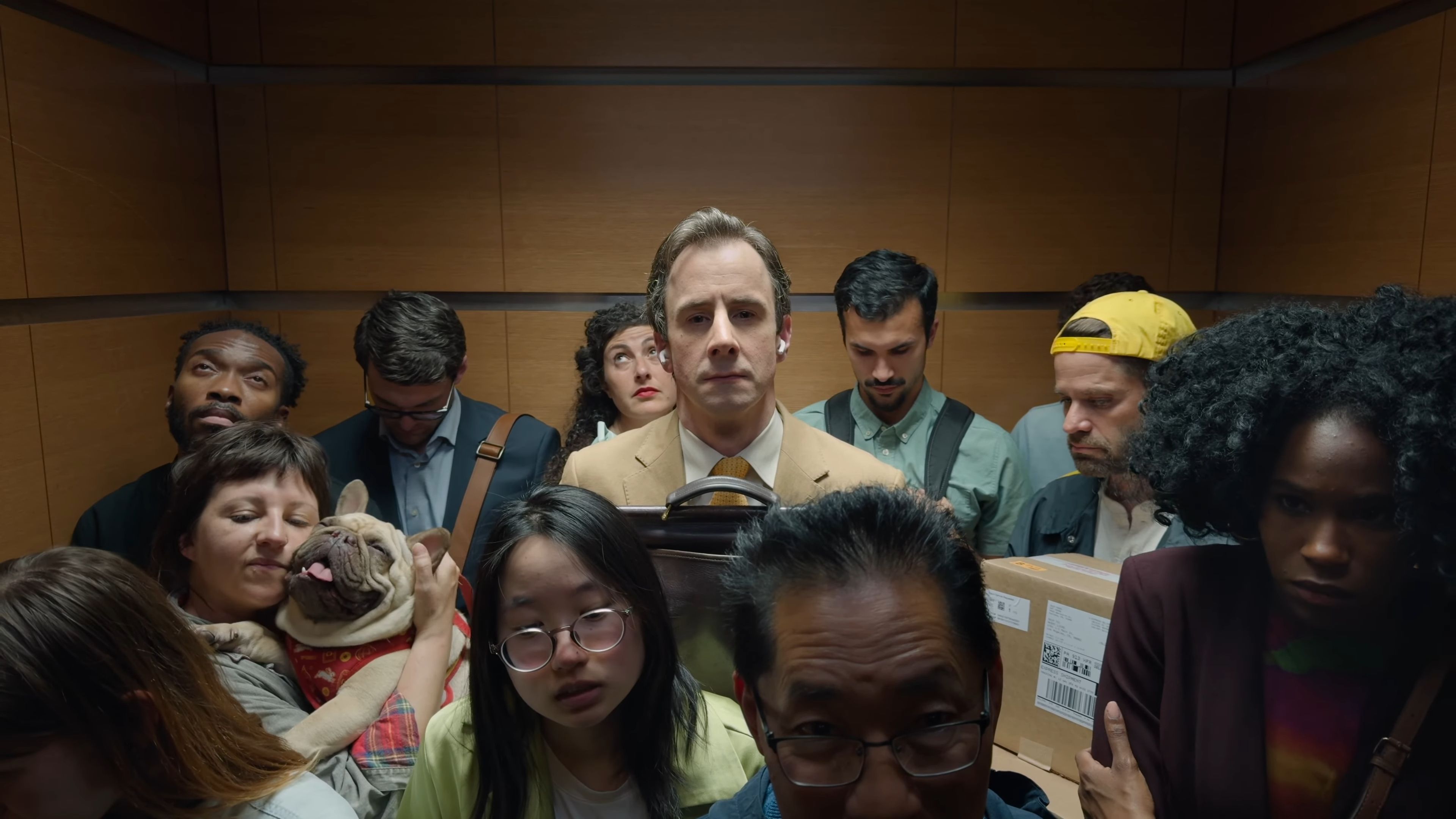 Man wearing AirPods standing in an elevator, surrounded by ten other people.