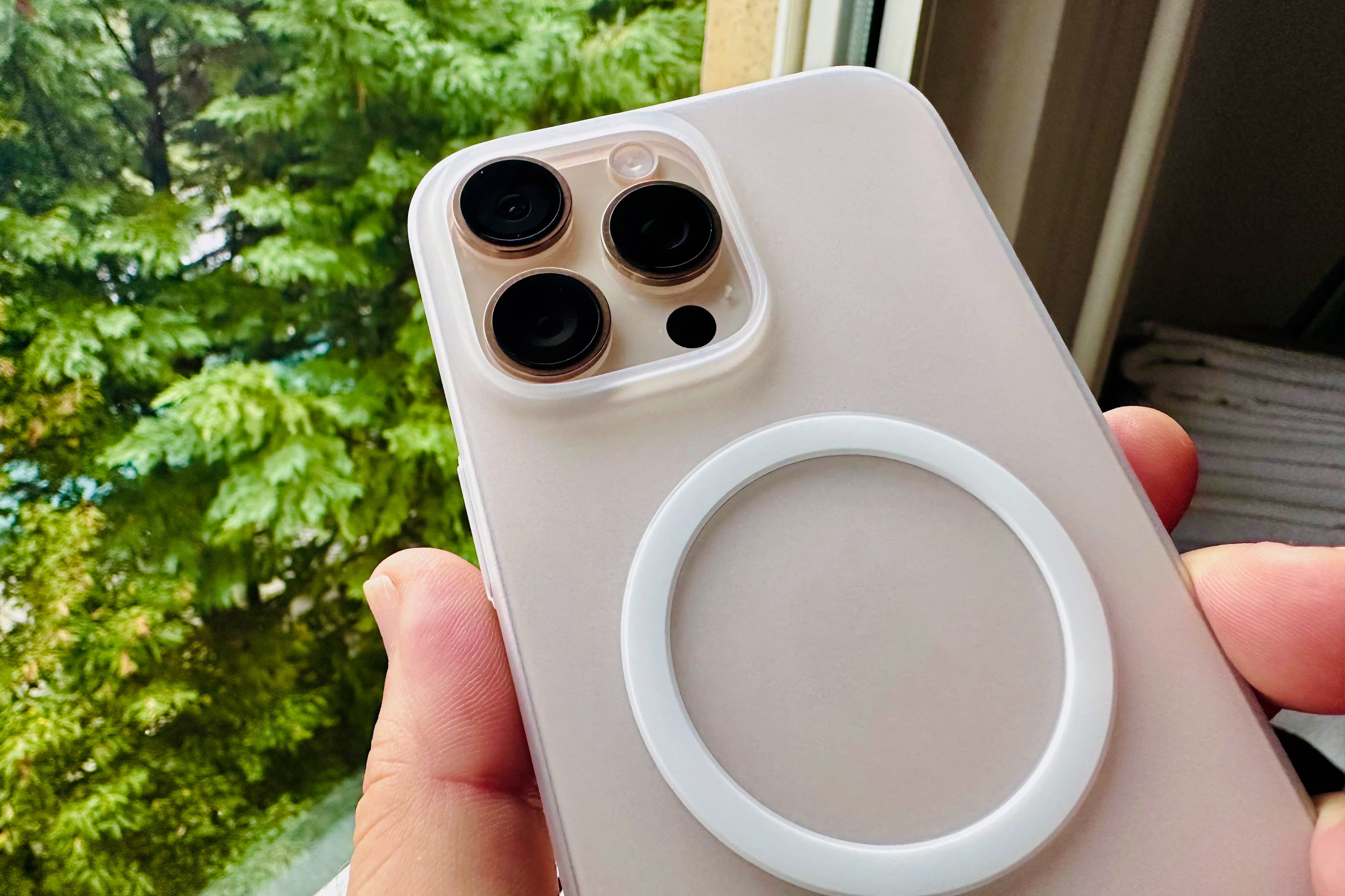 Hand holding an iPhone 16 Pro Max in a Totallee MagSafe clear case at a window, showcasing the rear cameras.