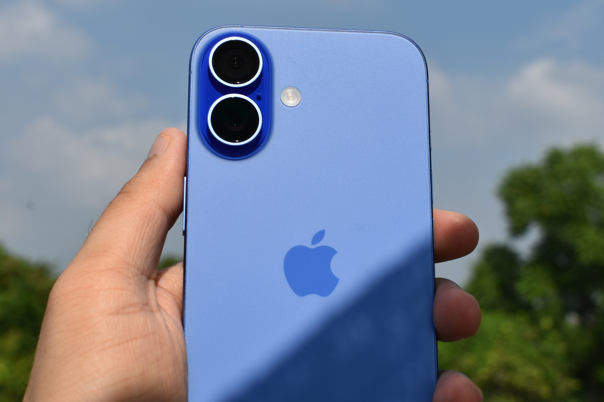 iPhone 16 in Ultramarine color held in hand with the sky in the background.