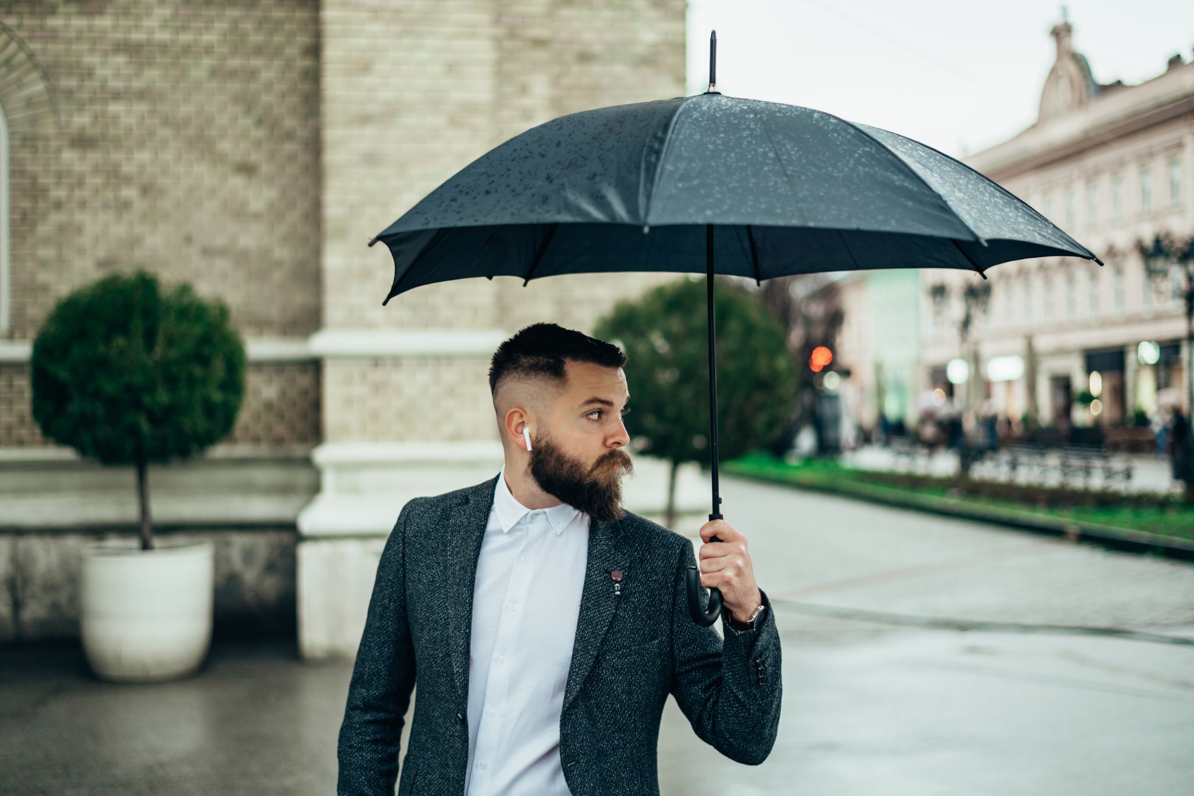 Man wearing AirPods in the rain under an umbrella.