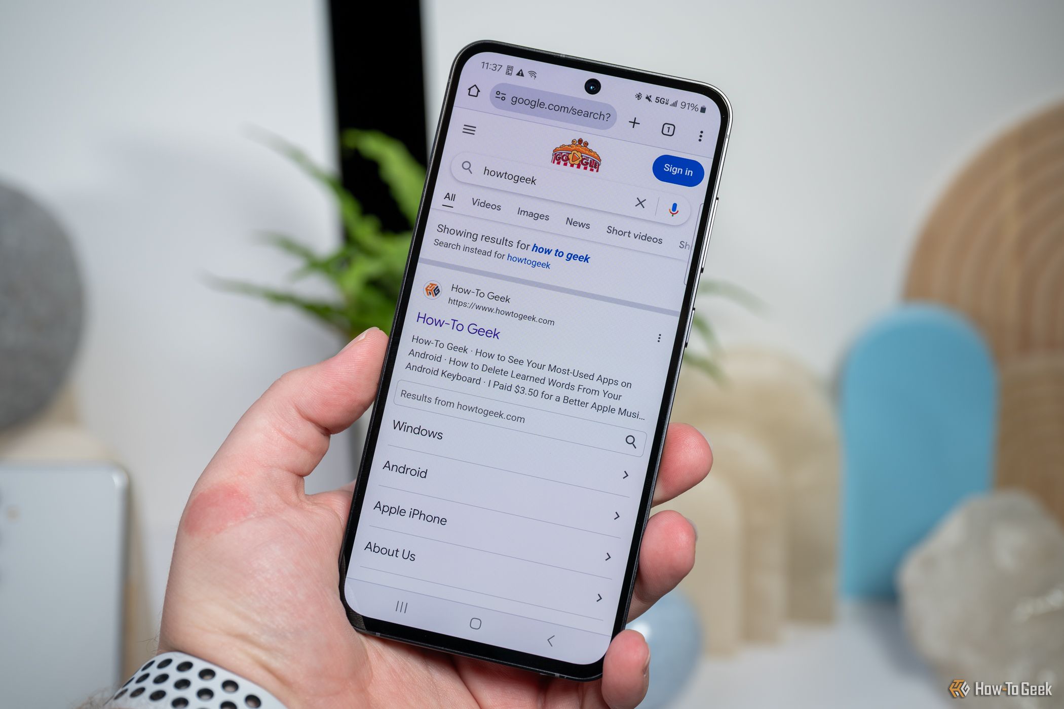 Person holding the Samsung Galaxy S24 FE showing How-To Geek Google results