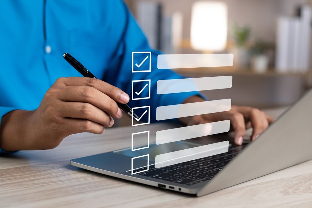 A man holding a pen in front of a laptop with a partially complete checklist floating above the keyboard.