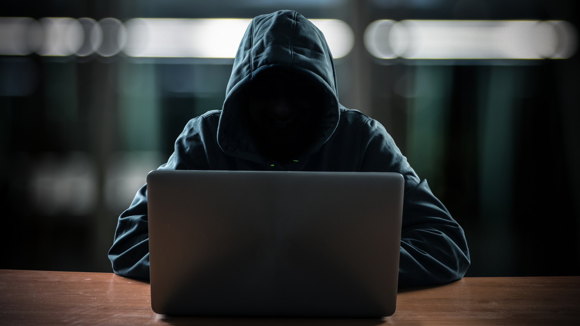 Hacker in front of his computer with a dark face.