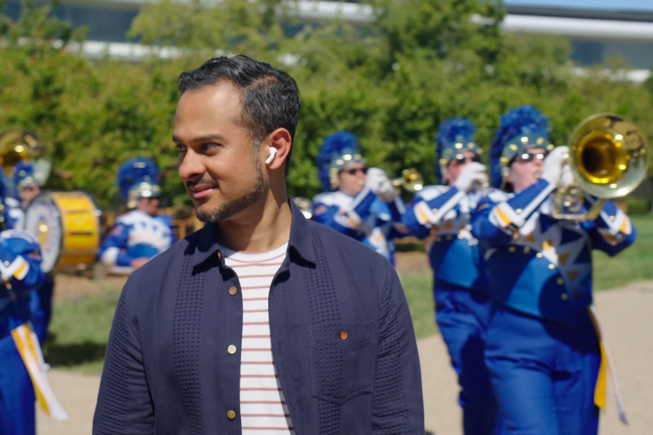 Young man walking in the park, listening to his AirPods while surrounded by trumpeters and horn players