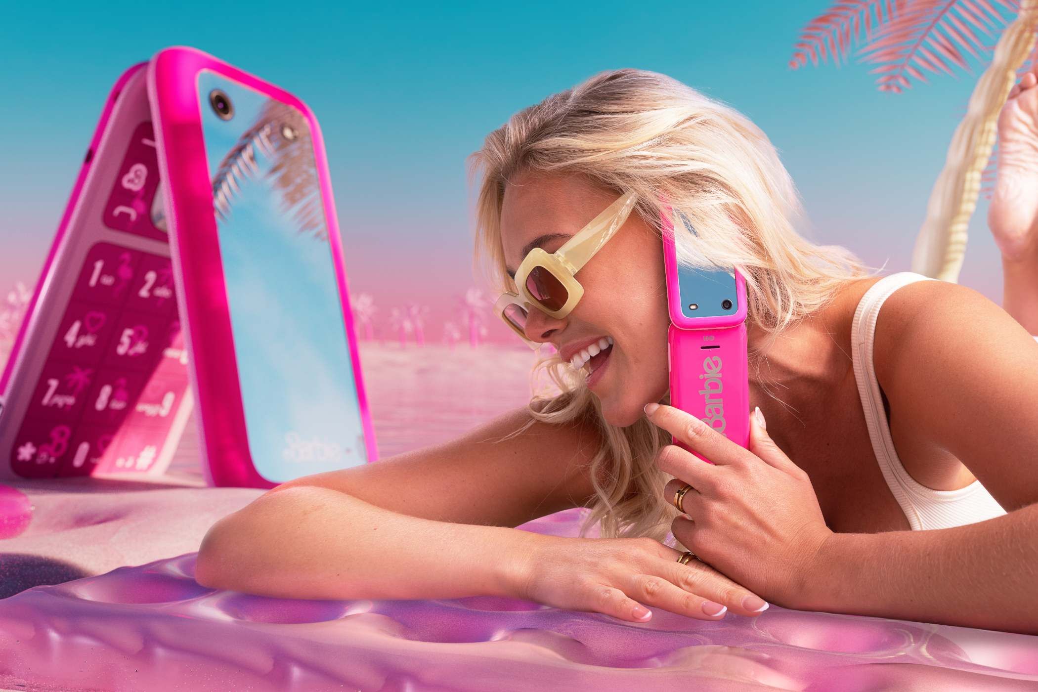 pink Barbie phone being used on the beach near a larger flip phone with the same style