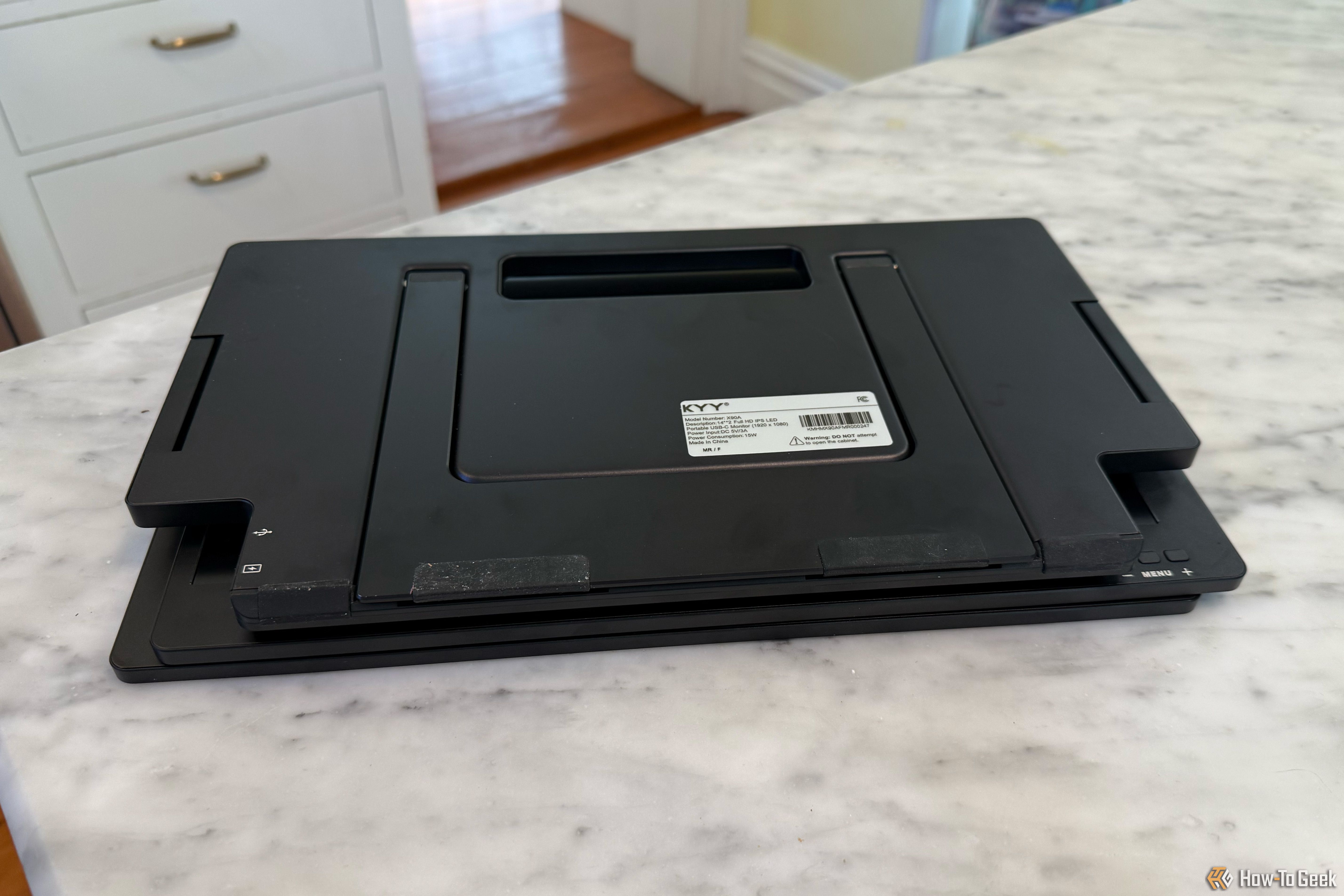 A marble table with a black, folded external monitor setup sitting on it.