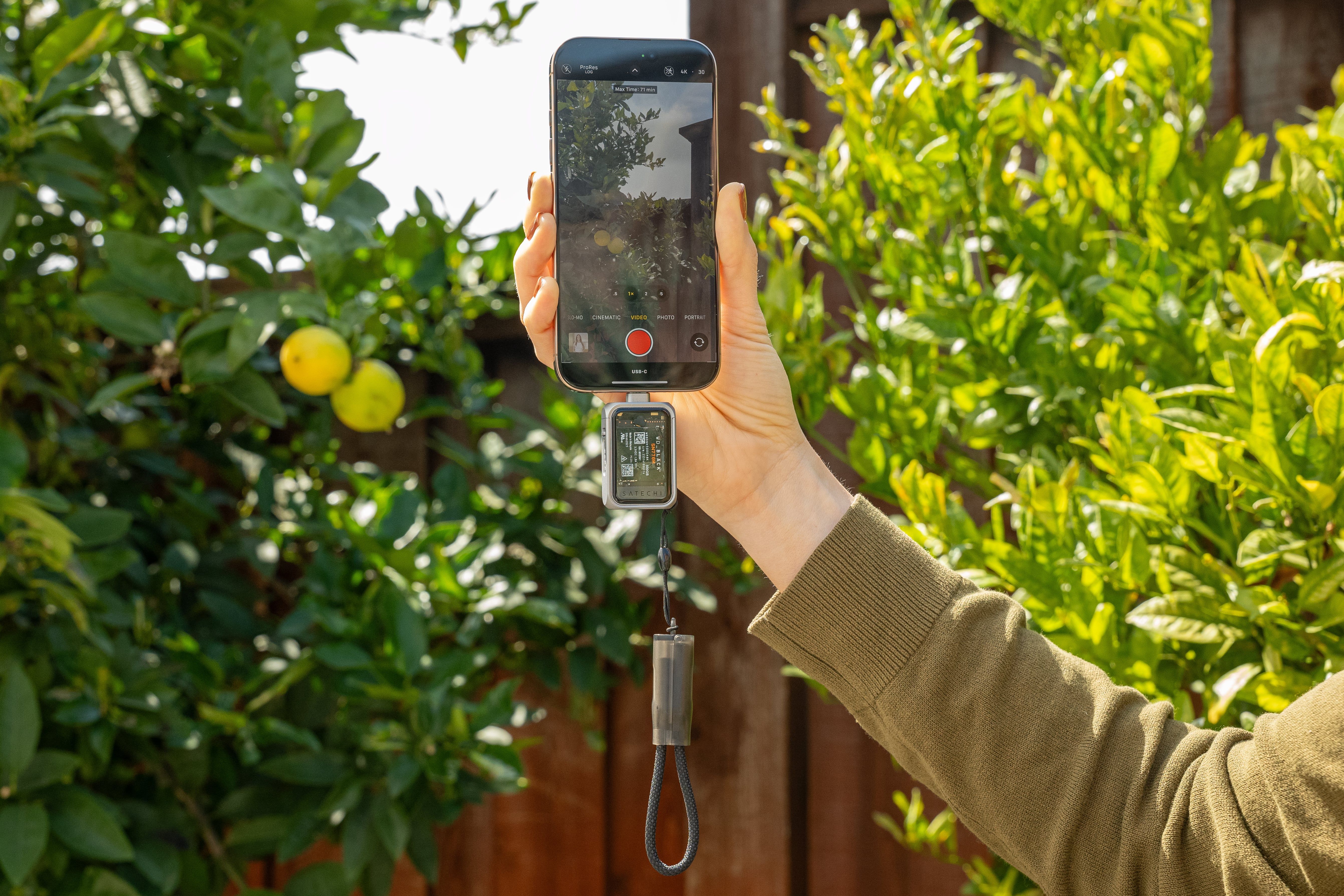 Hand holding an iPhone outside with a Satechi SSD enclosure attached to its USB-C port, recording a ProRes video.