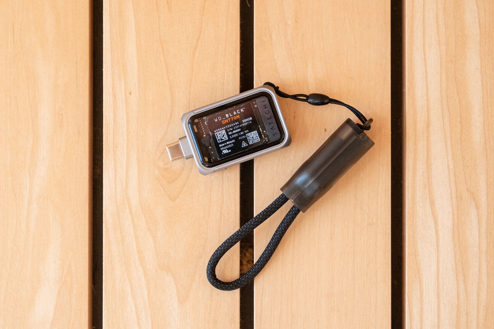 Top down view of Satechi's SSD enclosure with a lanyard on a wooden surface.