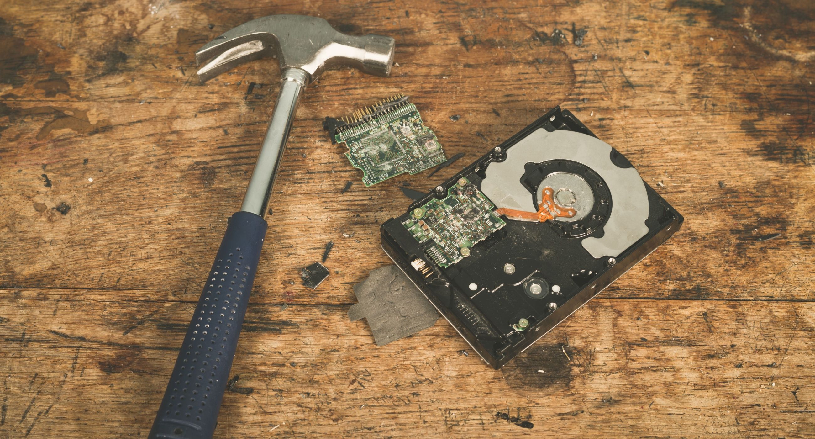 A hammer and a smashed computer harddrive on a wooden surface.