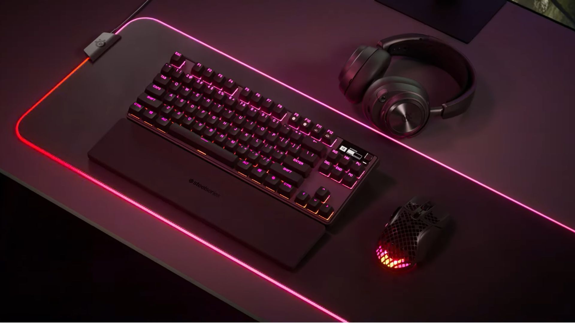 SteelSeries Apex Pro TKL on a gaming desk with red and pink lights.