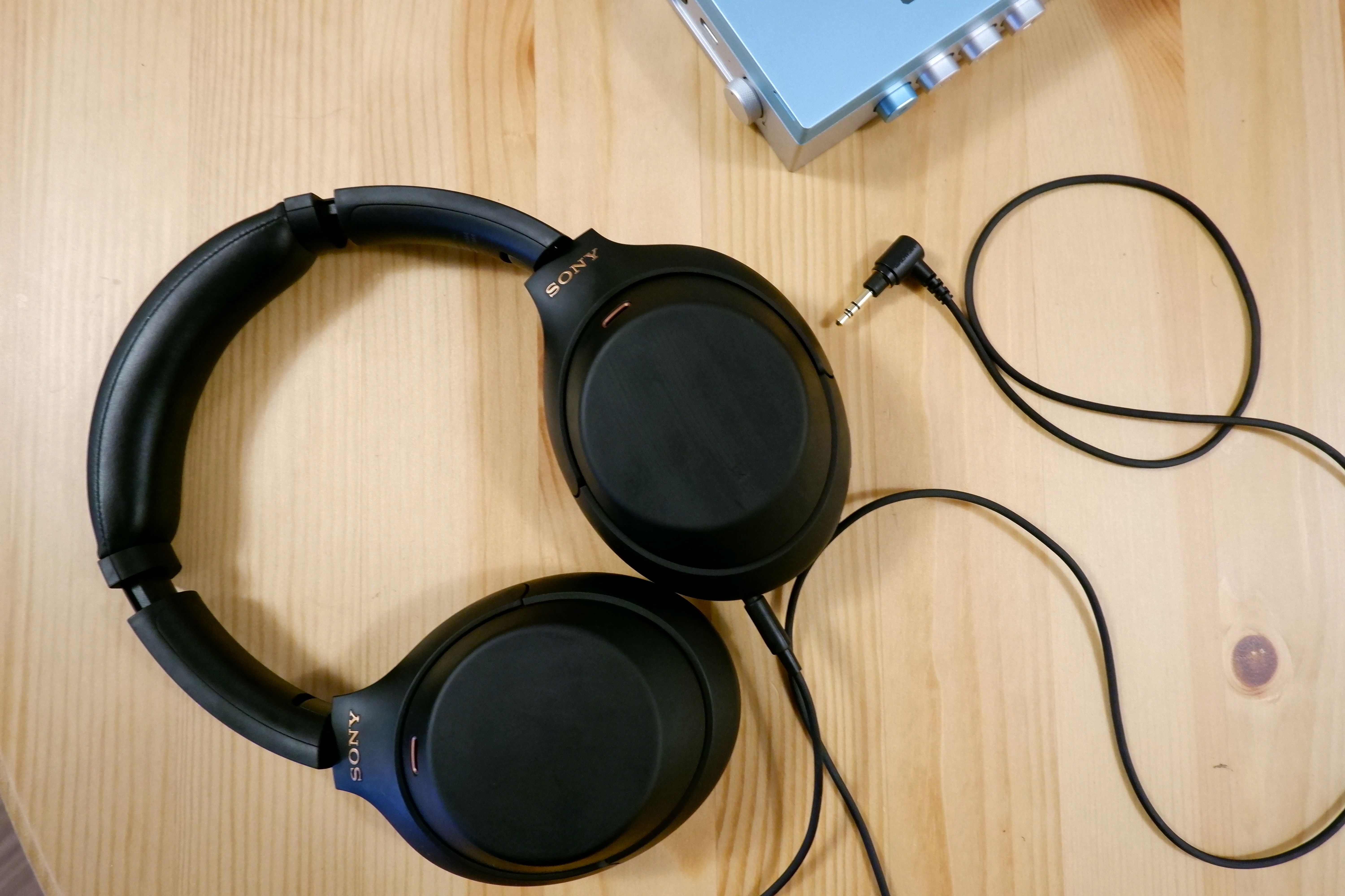 A pair of Sony WH-1000XM4 with the 3.5mm cable plugged in, on a wooden table.