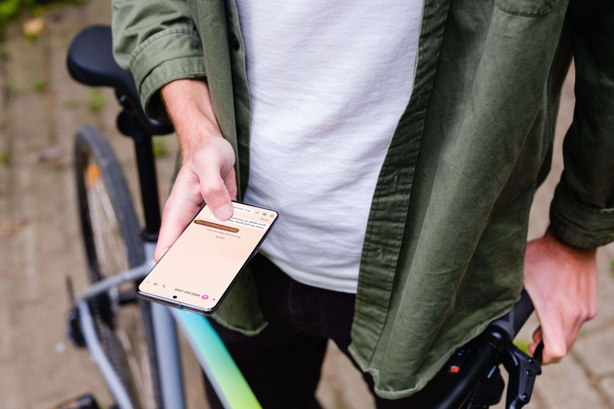 A person standing next to a bike holding their android device. There is a text conversation on the phone.