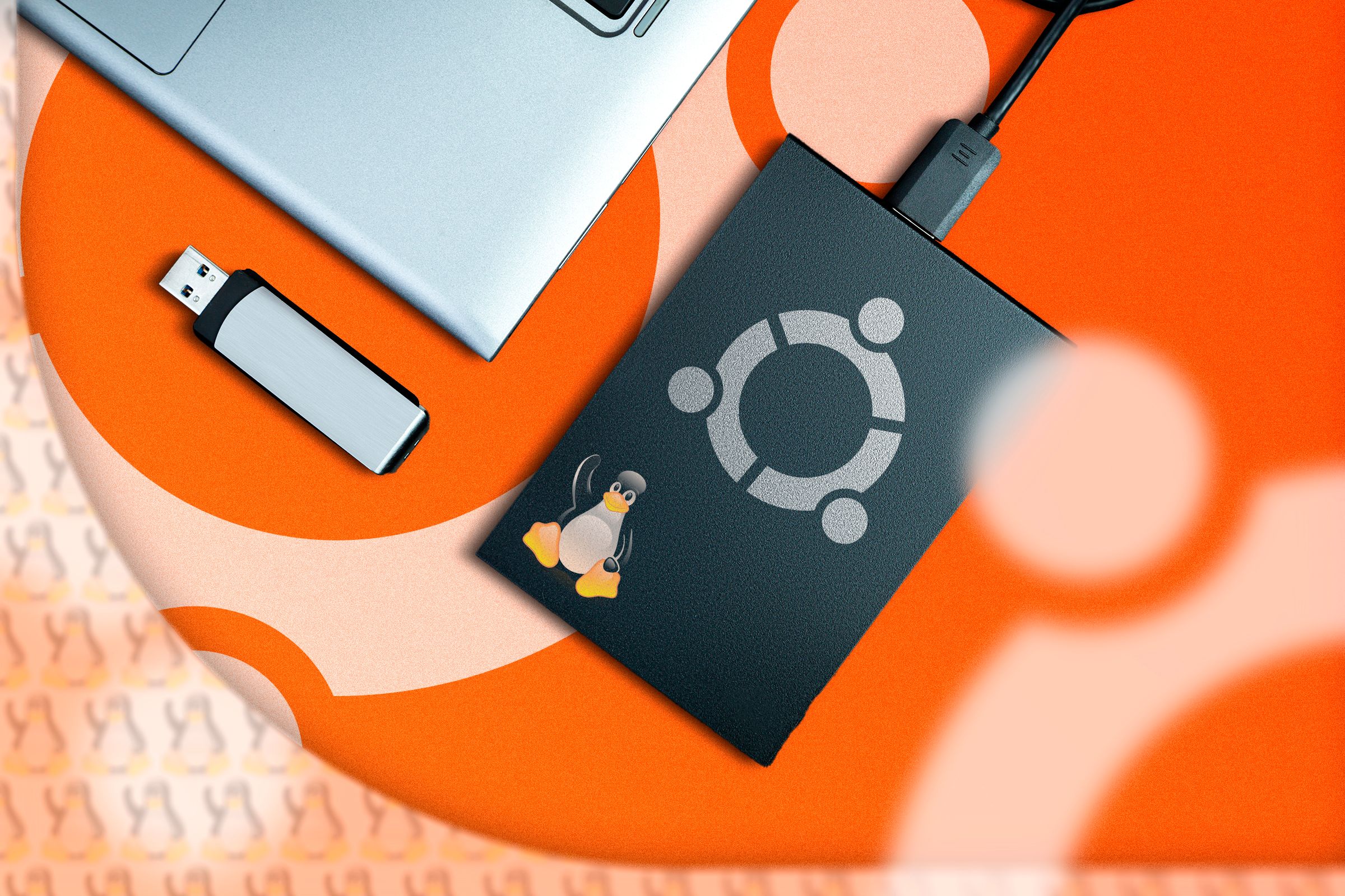 An external SSD with the Ubuntu logo connected to a laptop and a USB flash drive next to it.