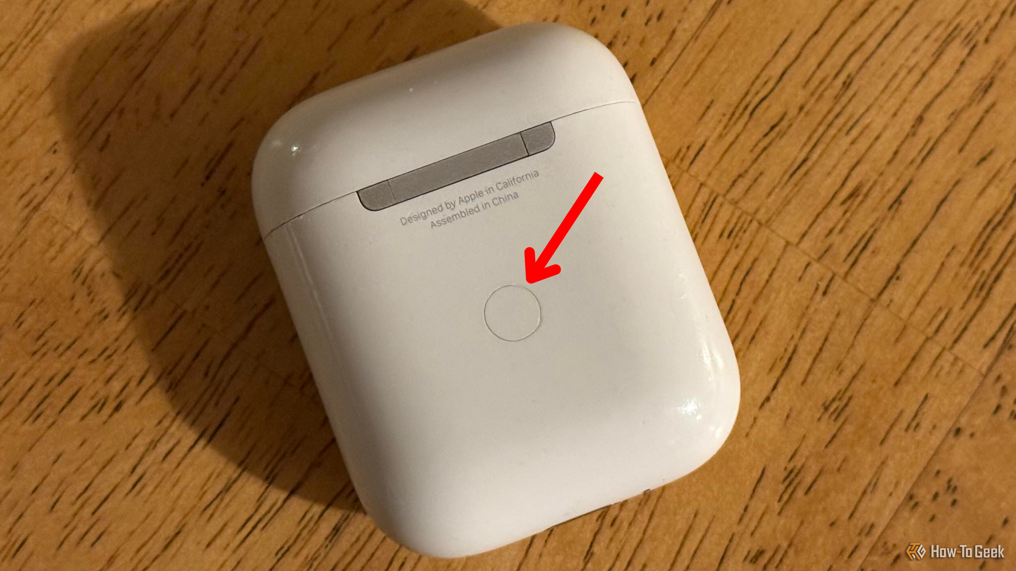 The back of an AirPods case with an arrow pointing to the pairing button.