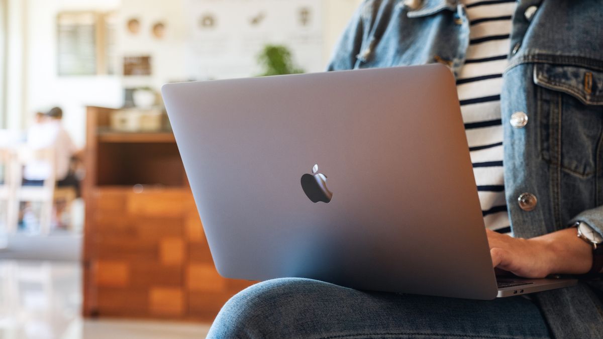 Person using a MacBook on their lap at a coffee shop