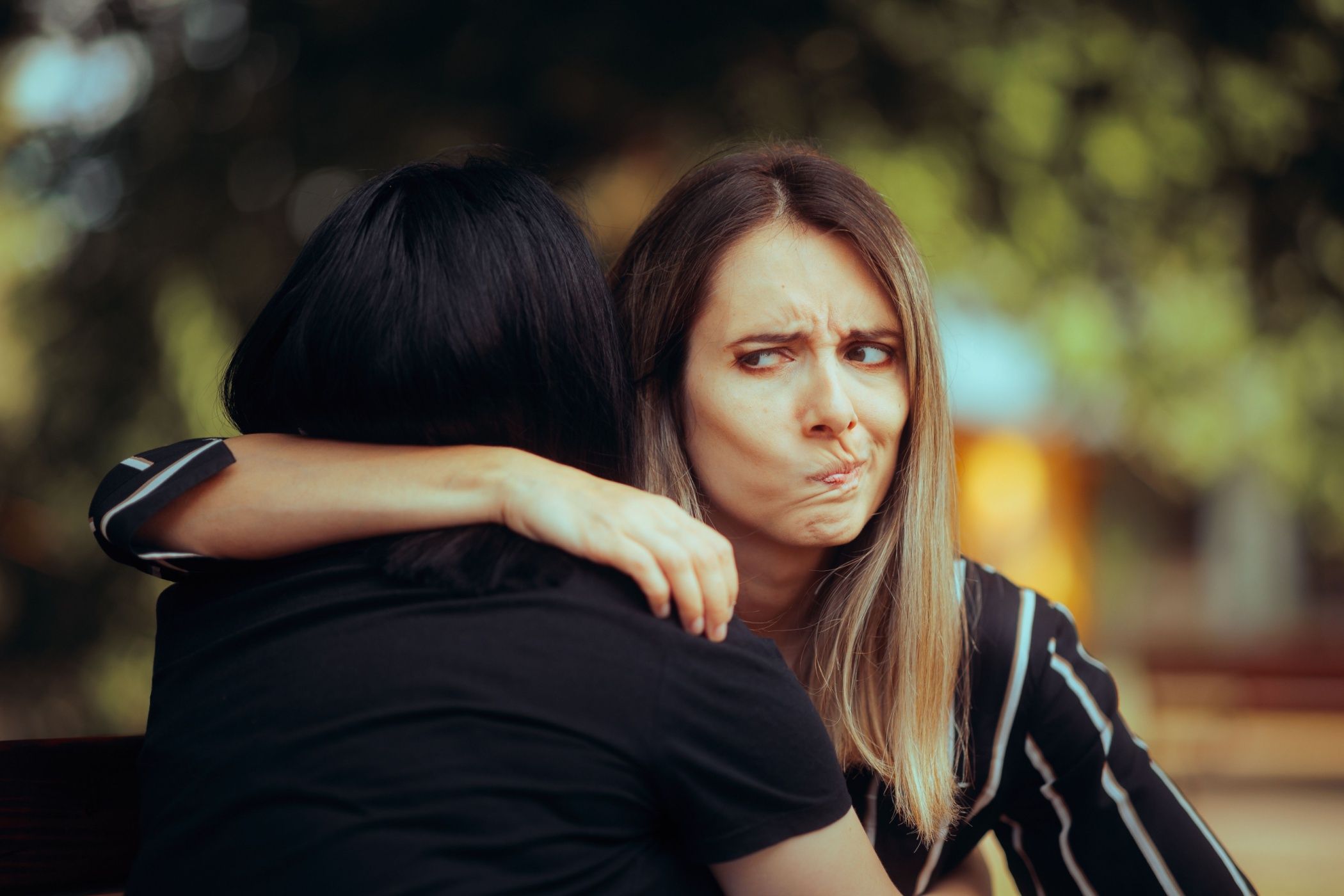 Woman hugs her fake friend, pulling a face behind her back.