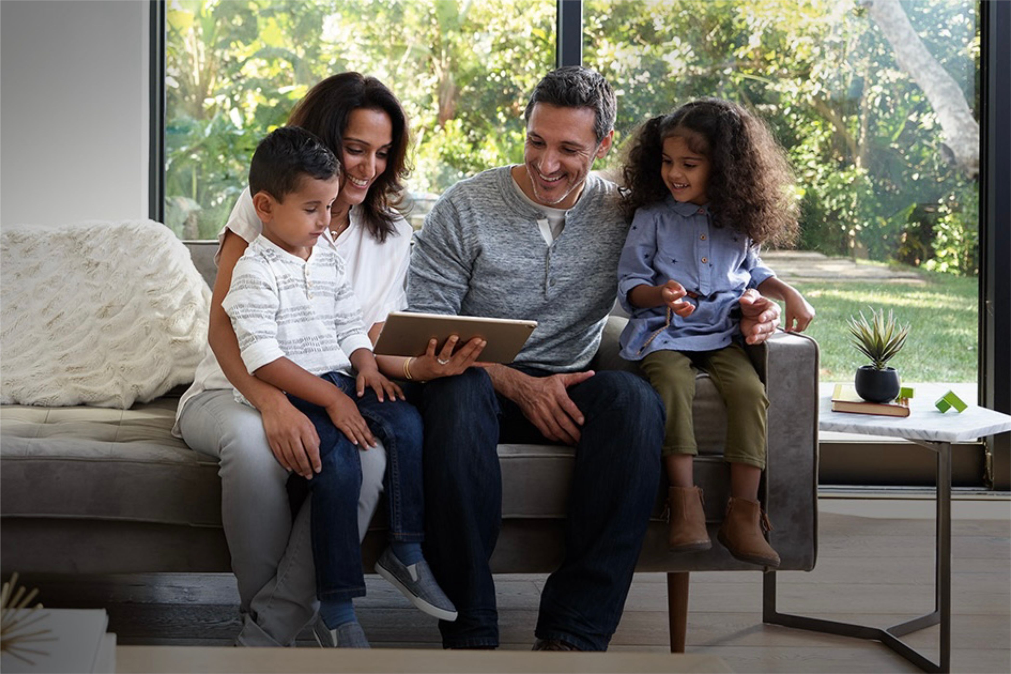 Two adults and two children gathering around an iPad while sitting on a couch.