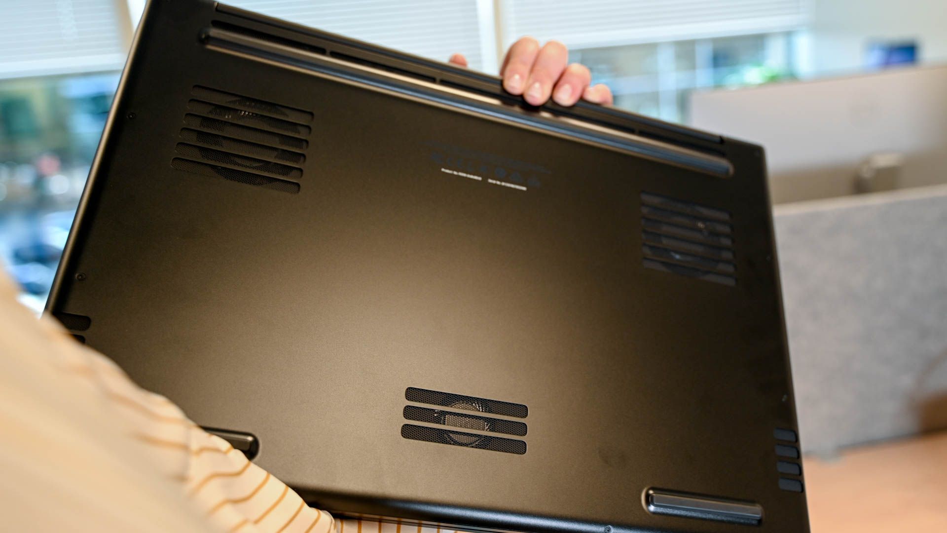 A person holding a laptop upside down in their hands.