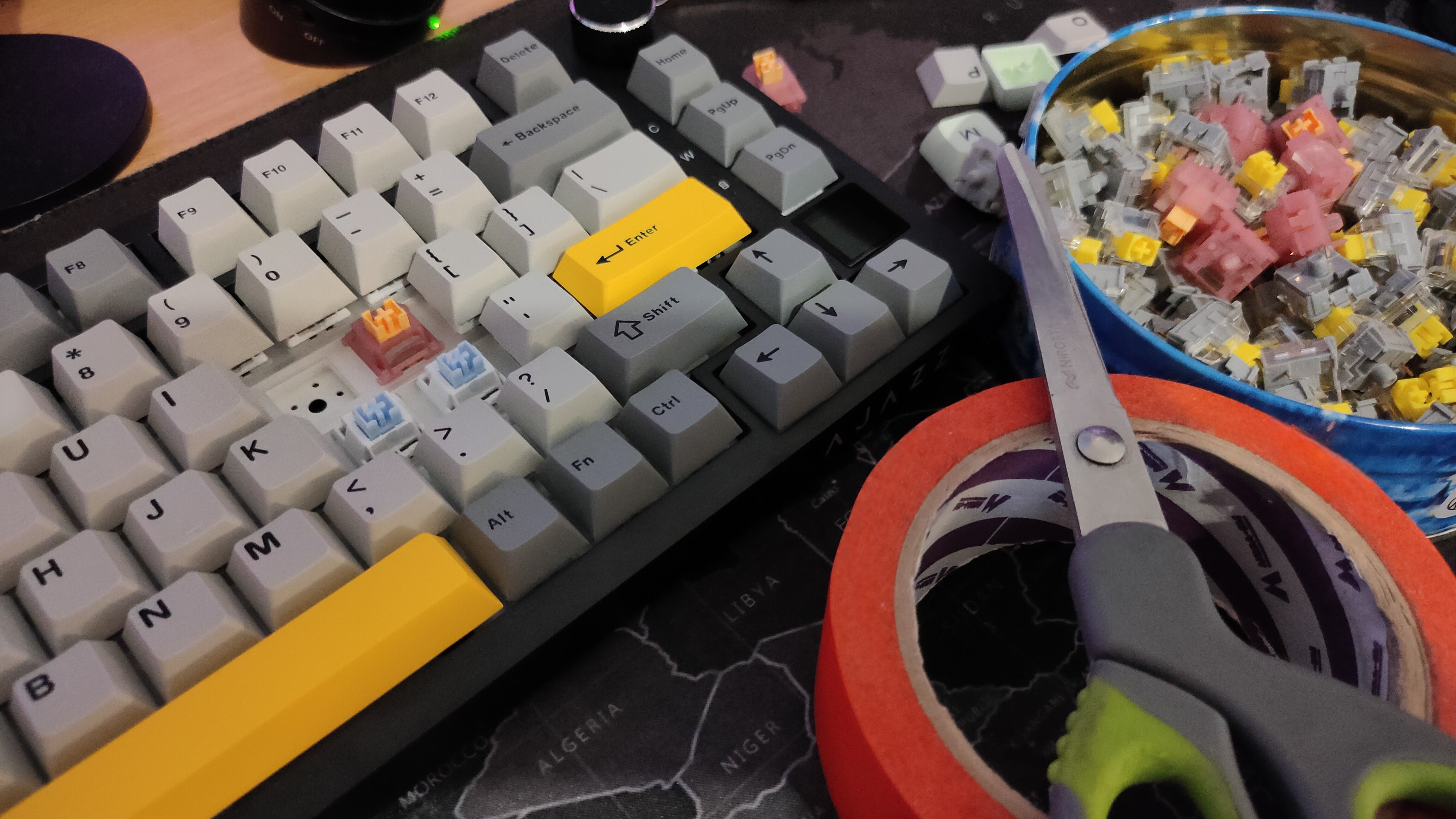 A mechanical keyboard with some painter's tape, scissors, and switches next to it.