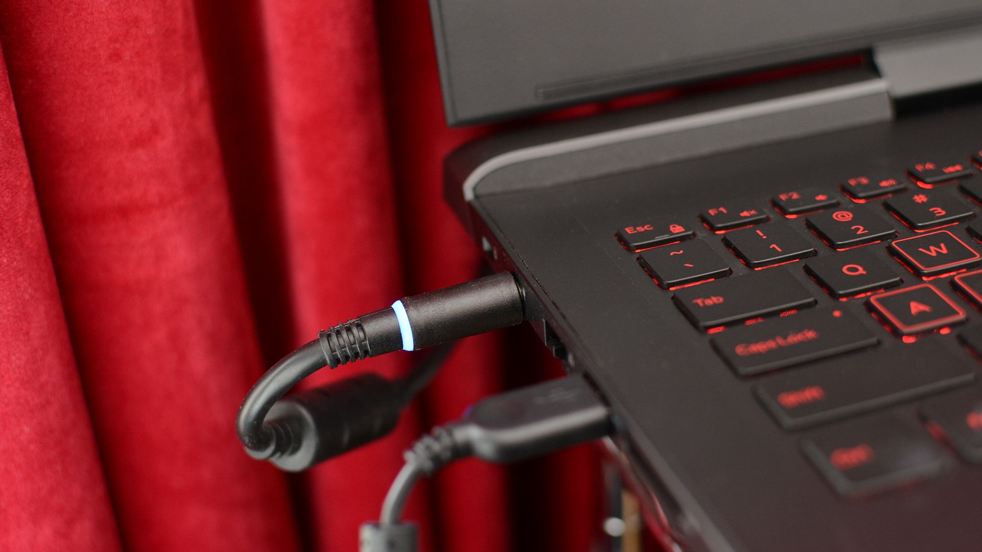 A charger plugged into a laptop placed close to a curtain.