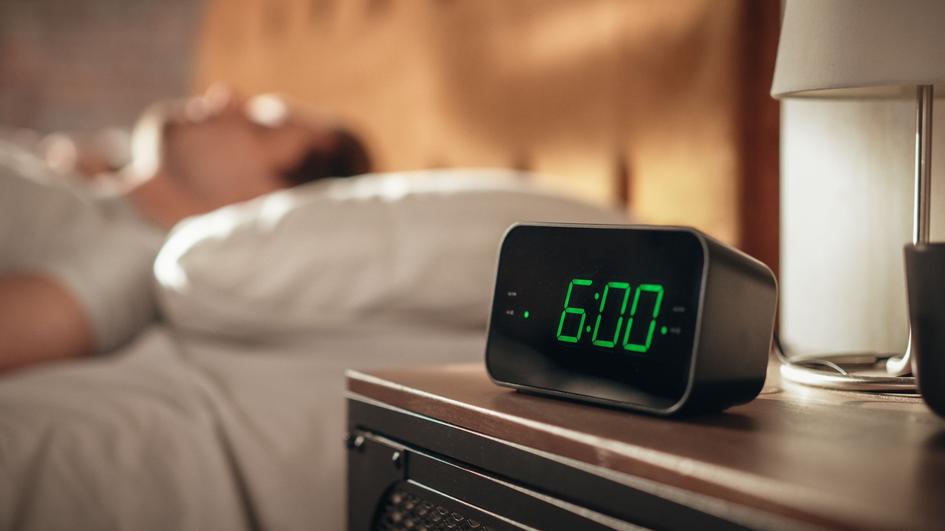 Man in bed next to alarm clock at 6am.