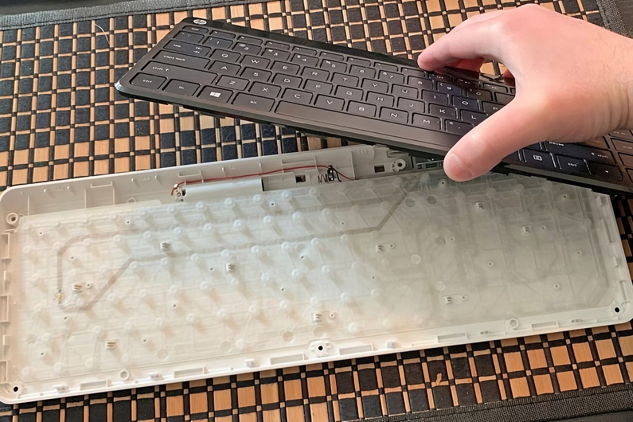 A membrane keyboard split into two parts with a hand holding the keycaps over the membrane.