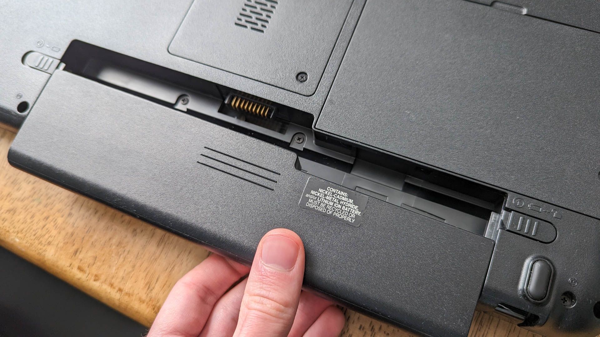 A person accessing the removable battery on a laptop