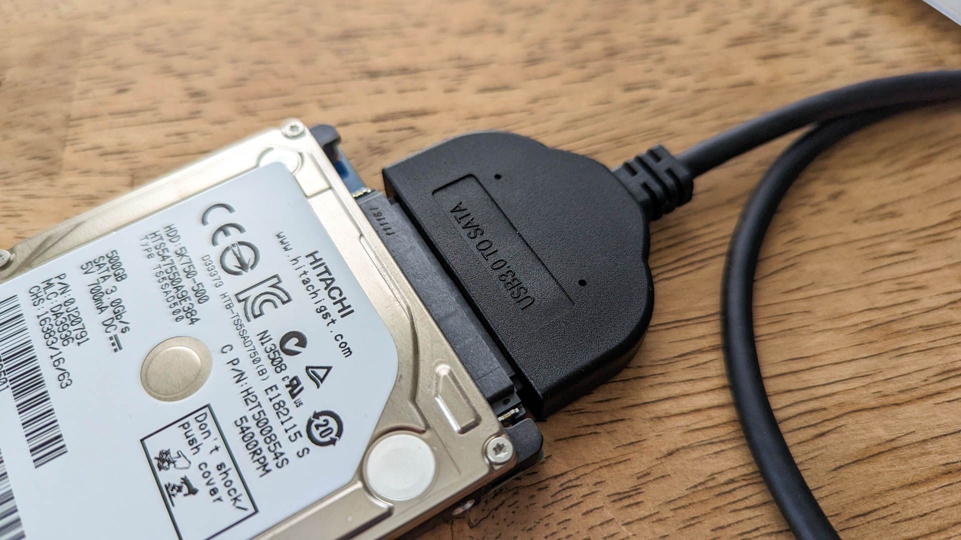 Hard drive connected to a USB adapter on a wooden surface.