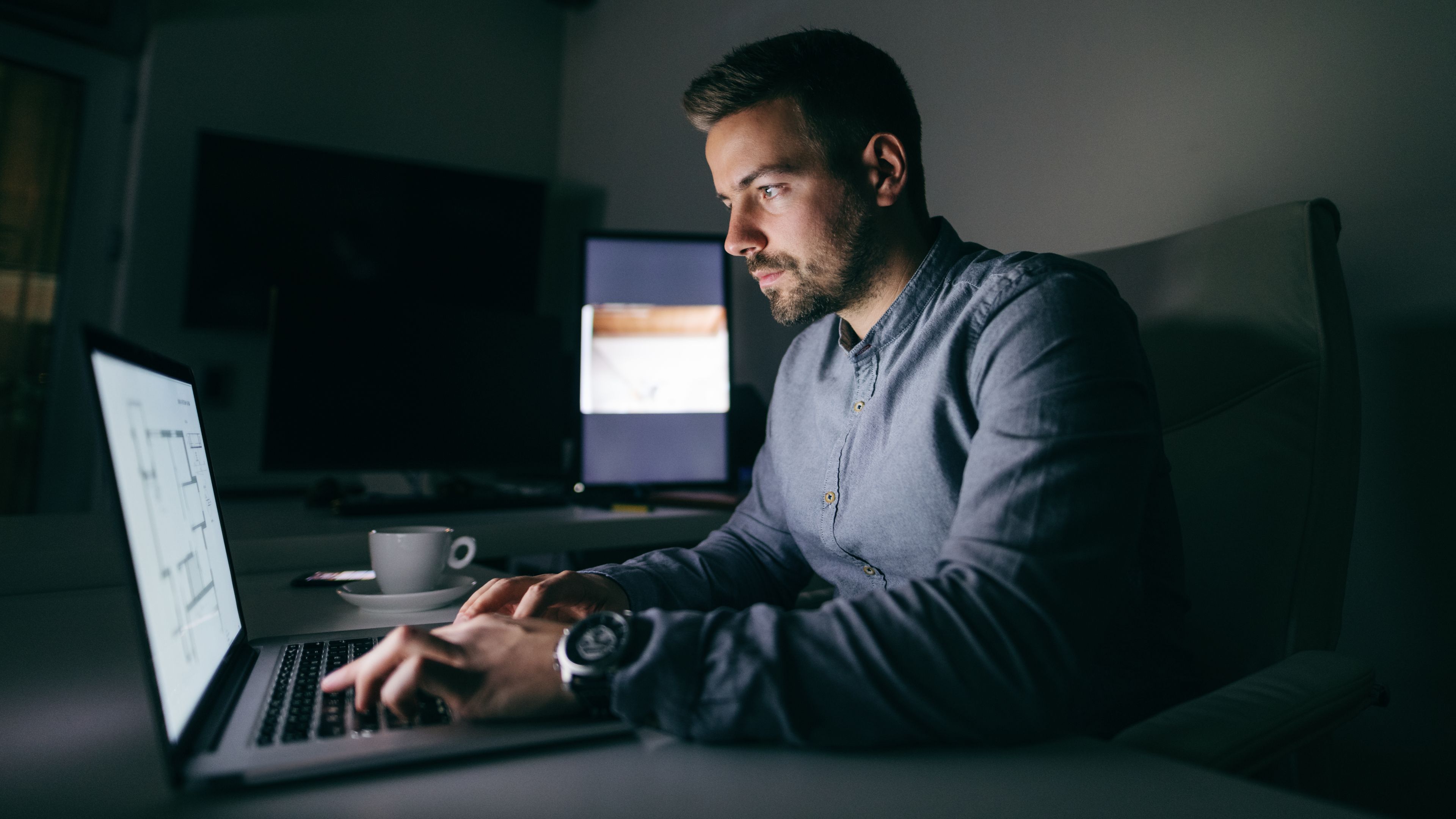 A man using a MacBook in a dark room at night.