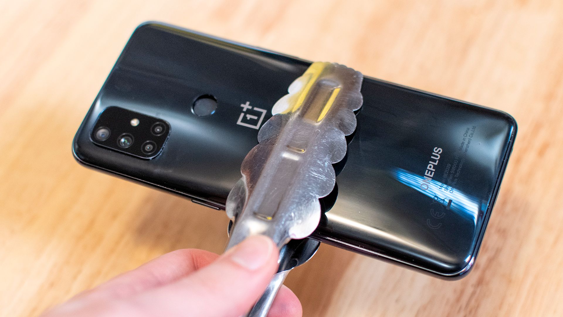 Holding a swollen OnePlus smartphone with a pair of kitchen tongs.