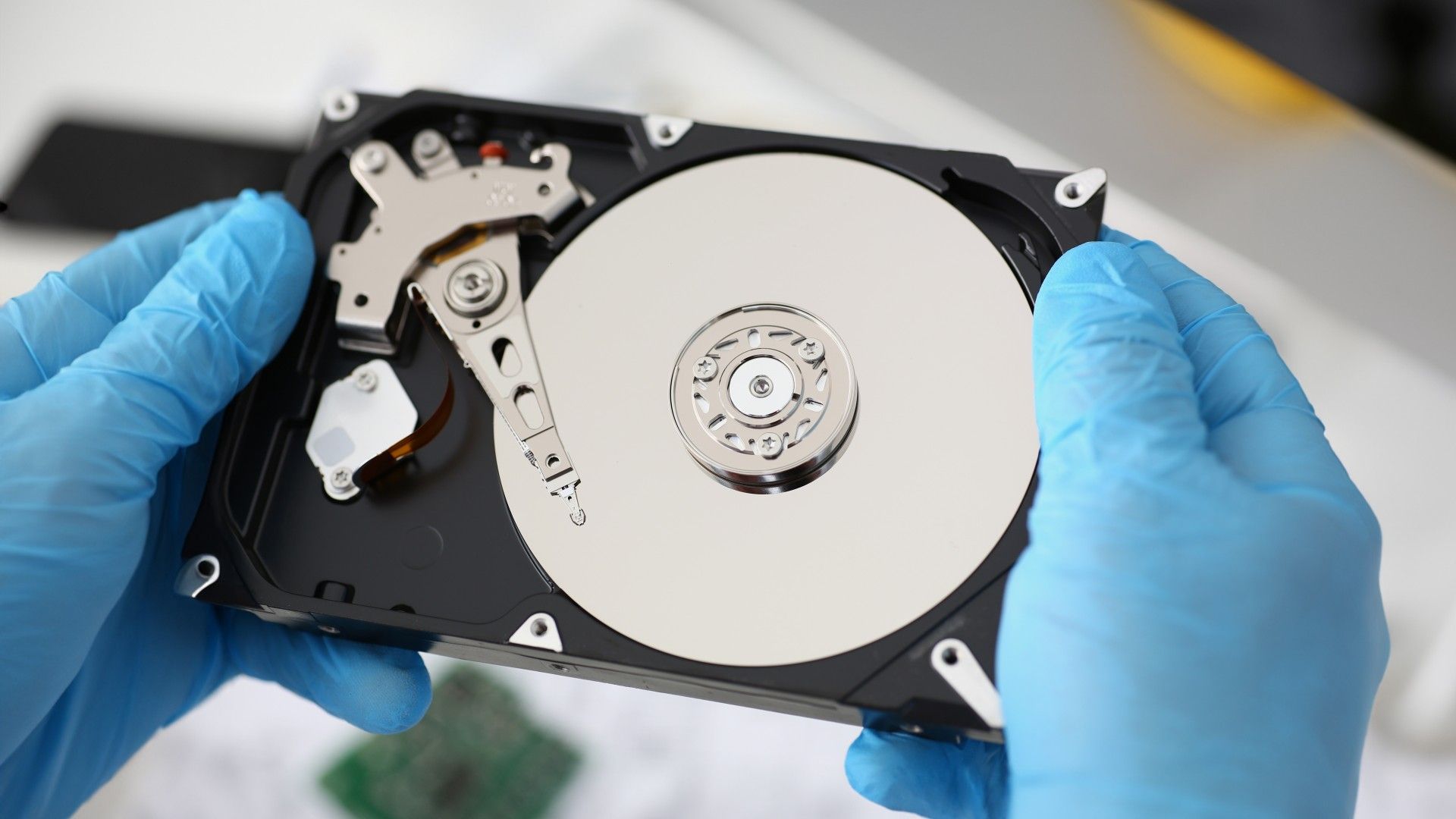 Close-up of a person's gloved hands holding a disassembled hard drive from computer.